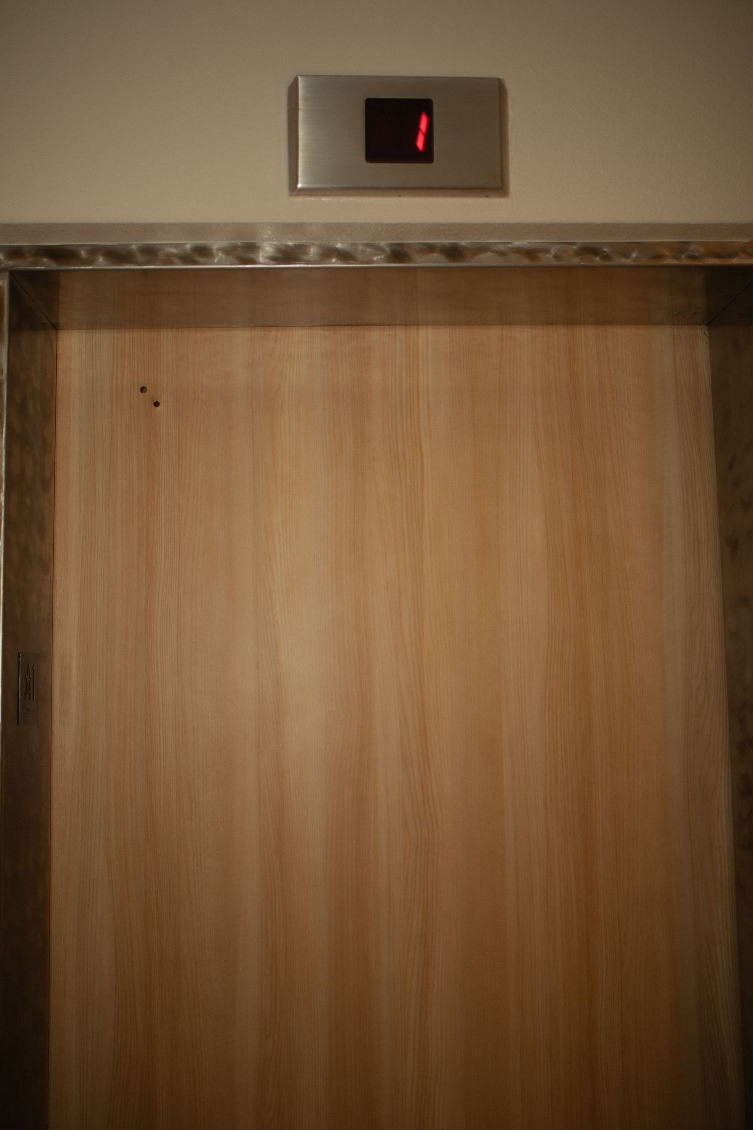 Closed wooden elevator doors with a red indicator light above in a modern building interior.