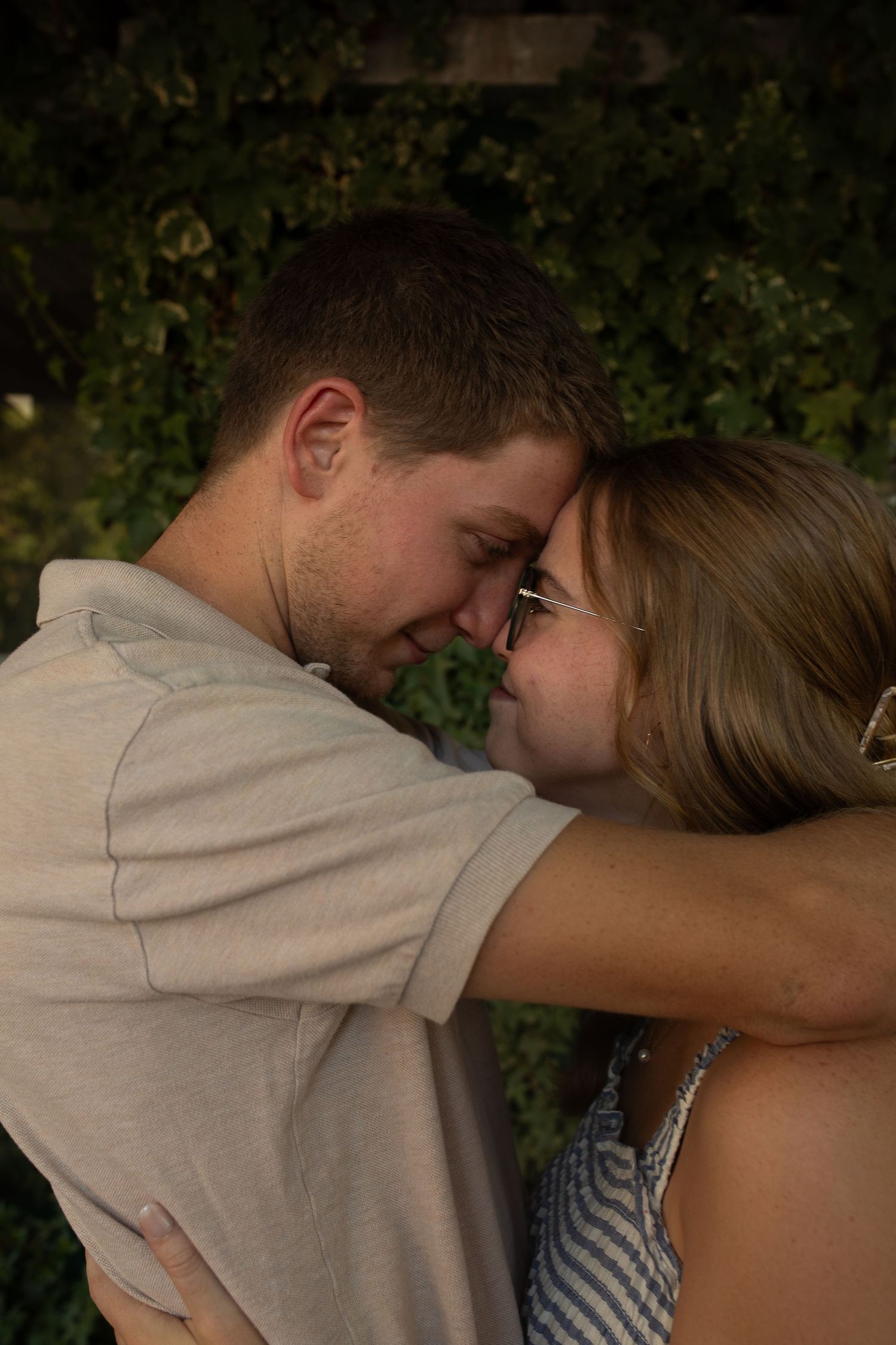 A romantic couple sharing an intimate moment outdoors at dusk with greenery in the background.