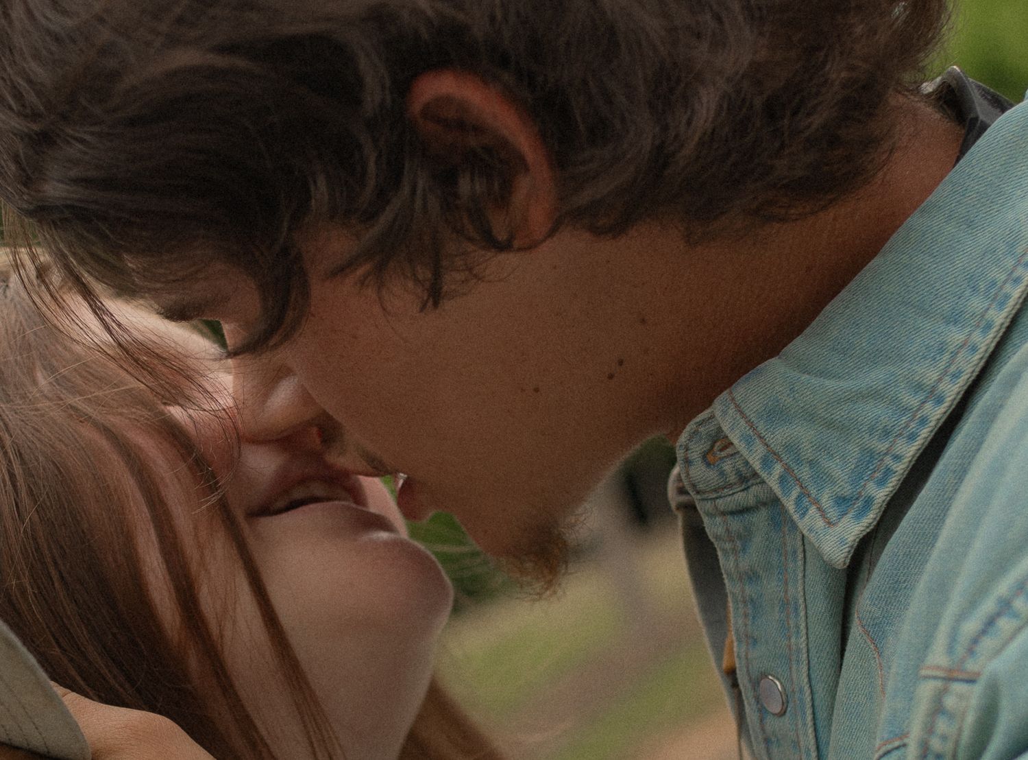 Two young people sharing a romantic kiss outdoors in natural light.