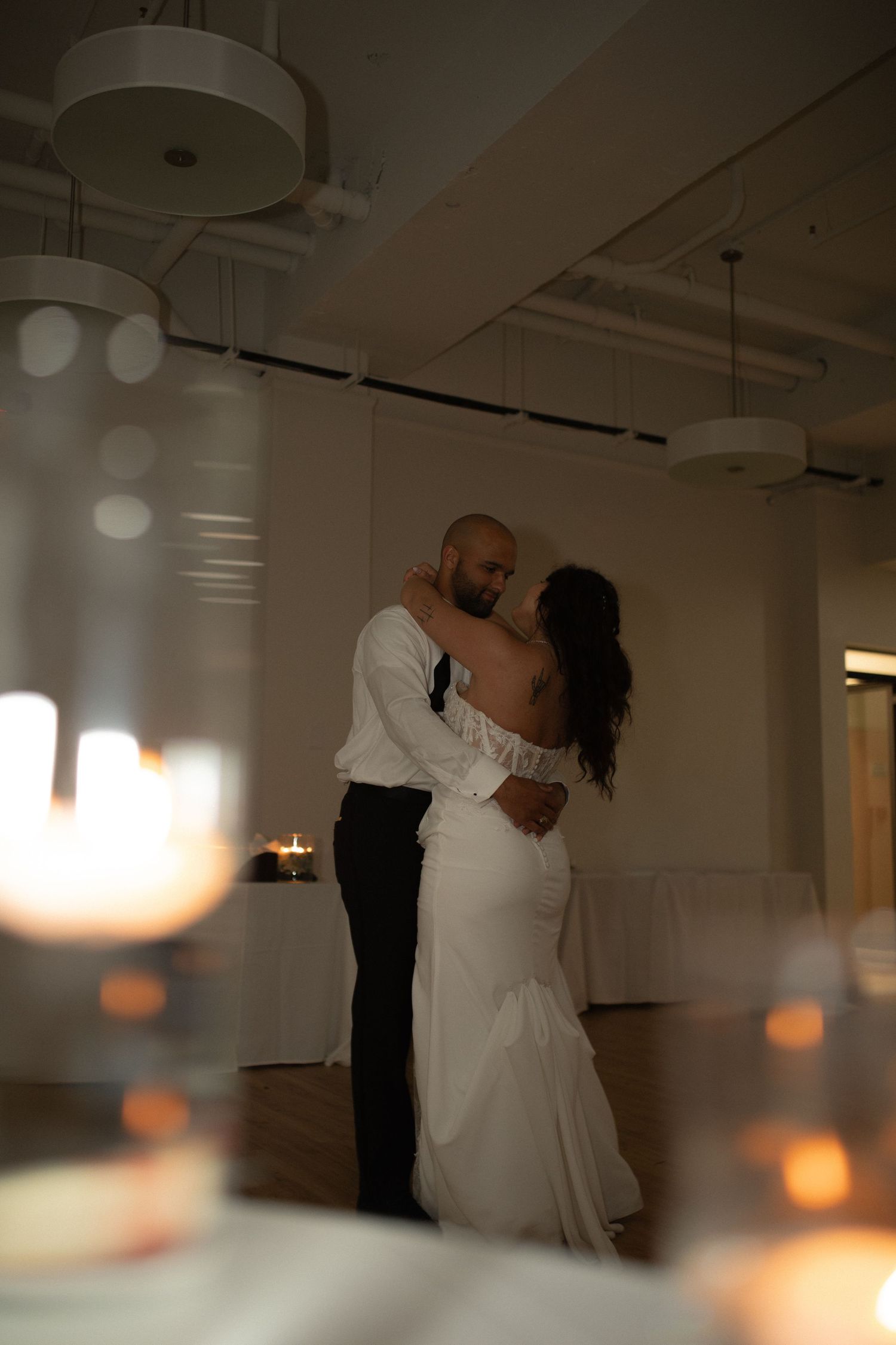 Bride and groom share their first dance in a softly lit wedding reception hall, framed by glowing candles.