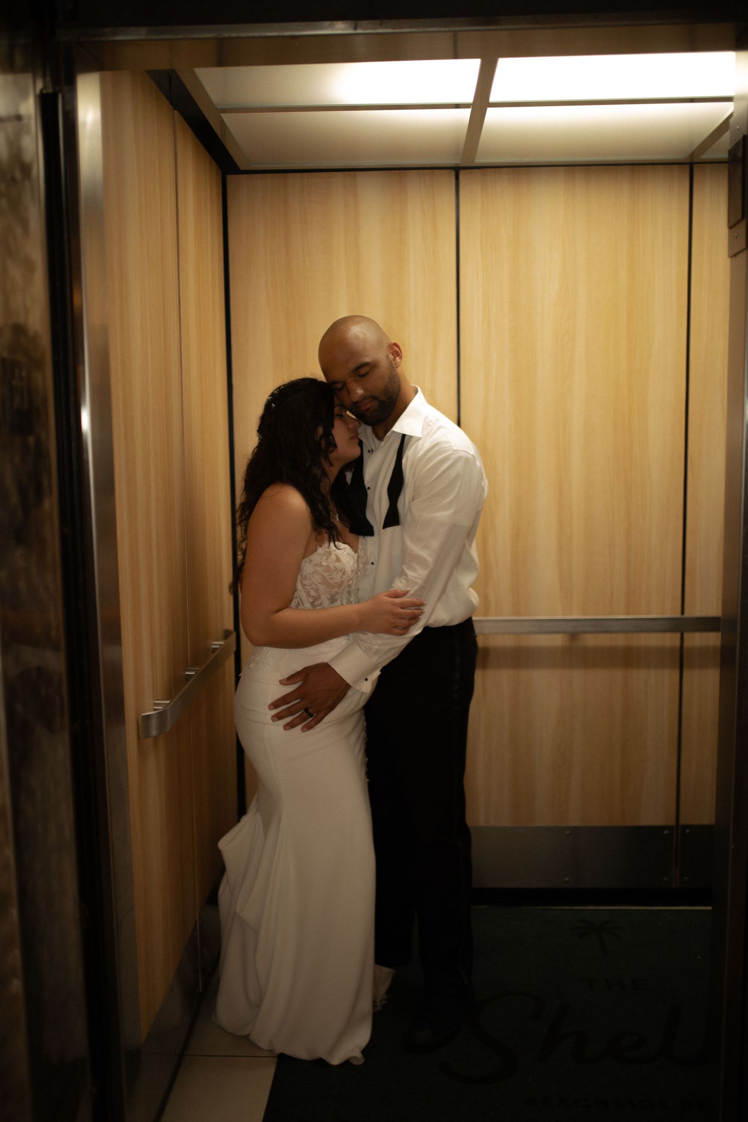 Bride and groom sharing a romantic embrace in a modern elevator, dressed in wedding attire.