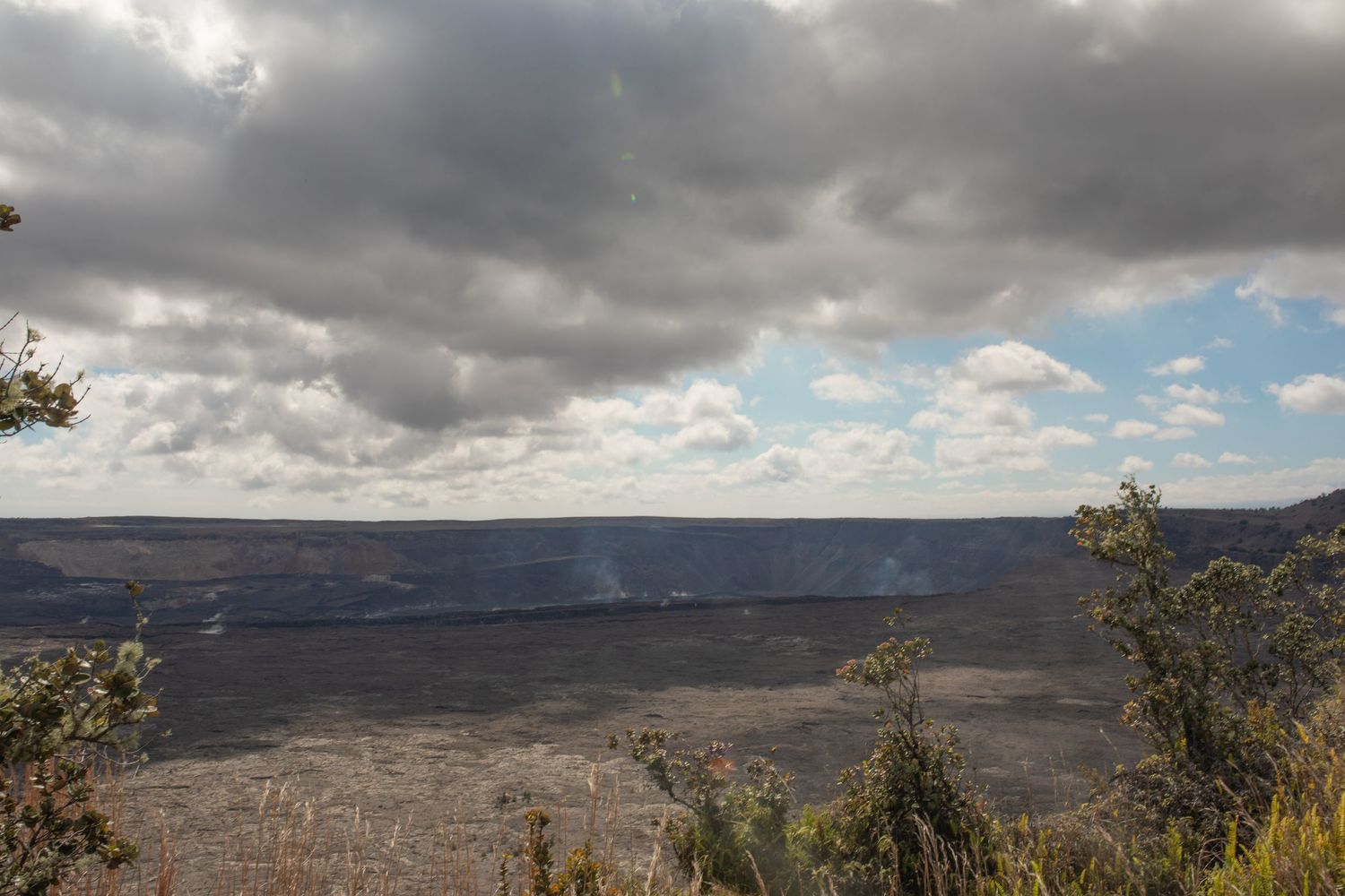A panoramic view of Kilauea Volcano in Hawaii with dark stormy clouds looming above the vast crater landscape.