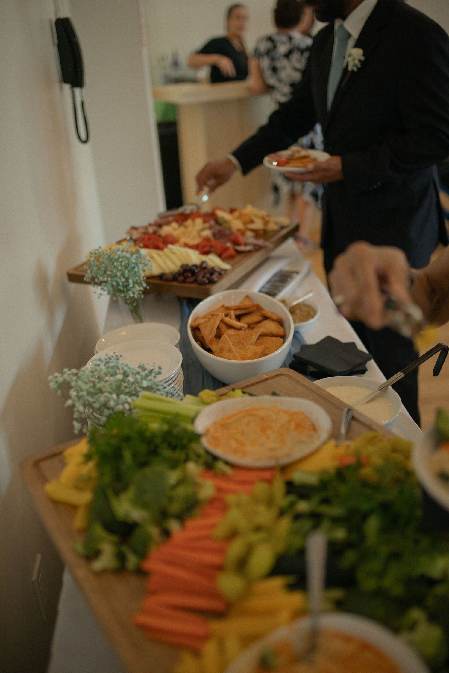 Elegant wedding reception buffet table with fresh vegetables, chips, dips, and charcuterie boards while guests serve themselves.