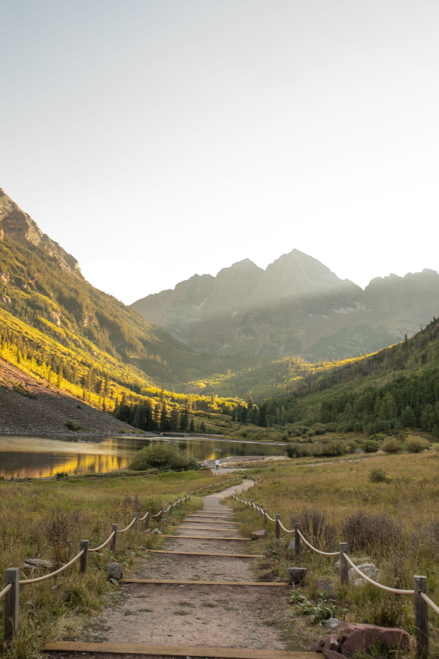 Wooden boardwalk trail leading to Maroon Bells peaks reflected in alpine lake, surrounded by fall foliage in Aspen, Colorado.