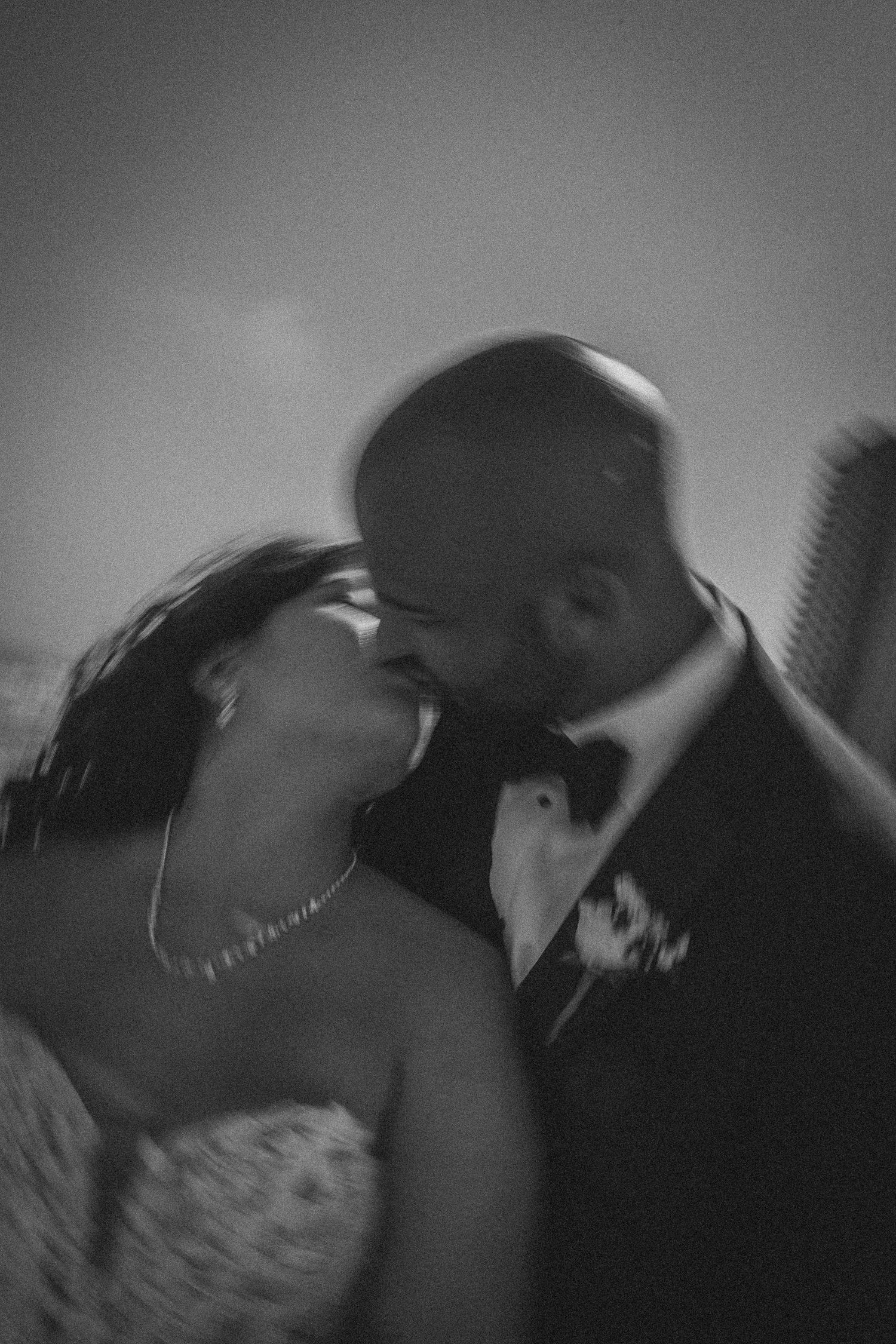 Black and white photo of bride and groom sharing a romantic kiss at their wedding ceremony.