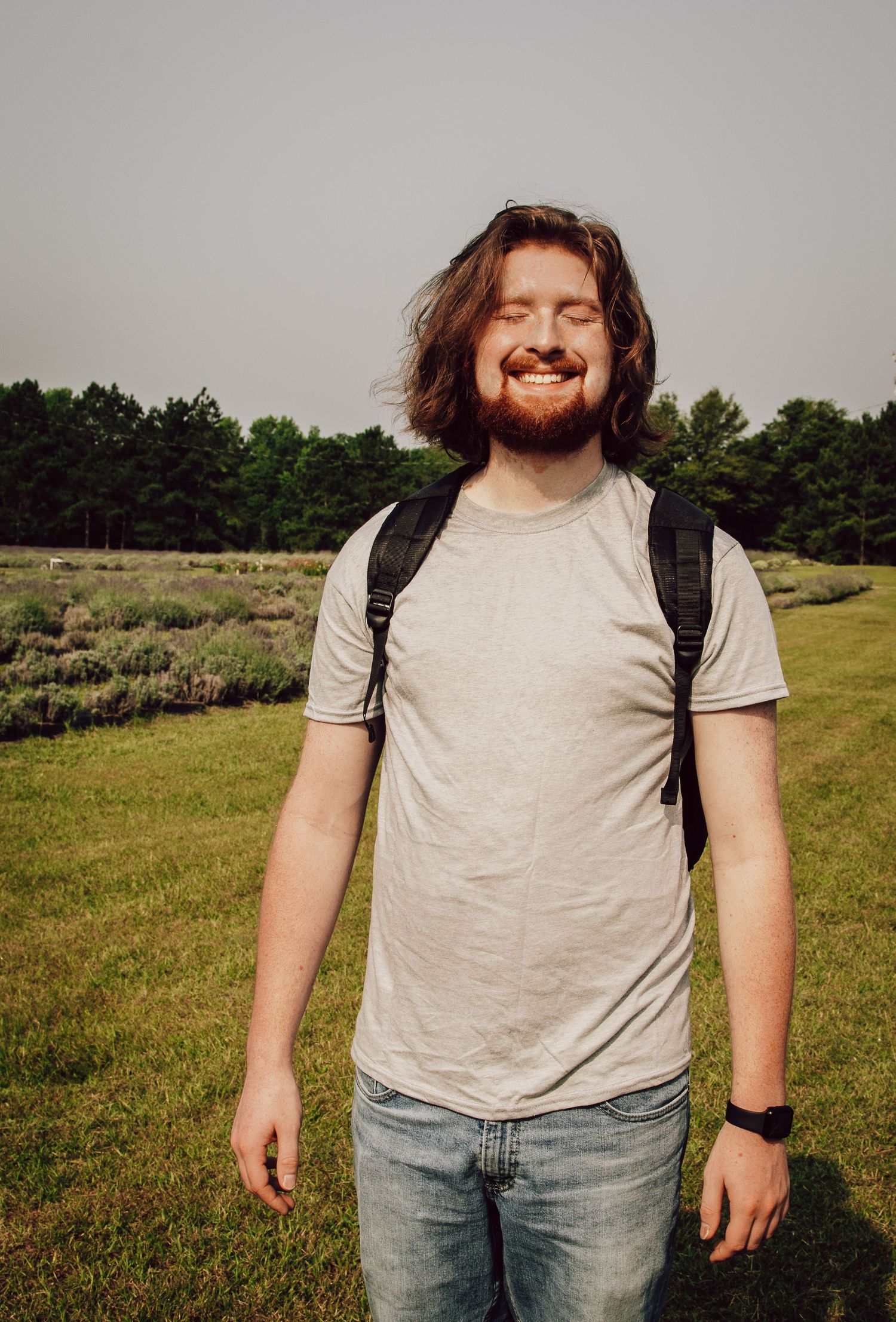 An outdoor portrait of someone wearing a backpack and casual attire in a grassy field.