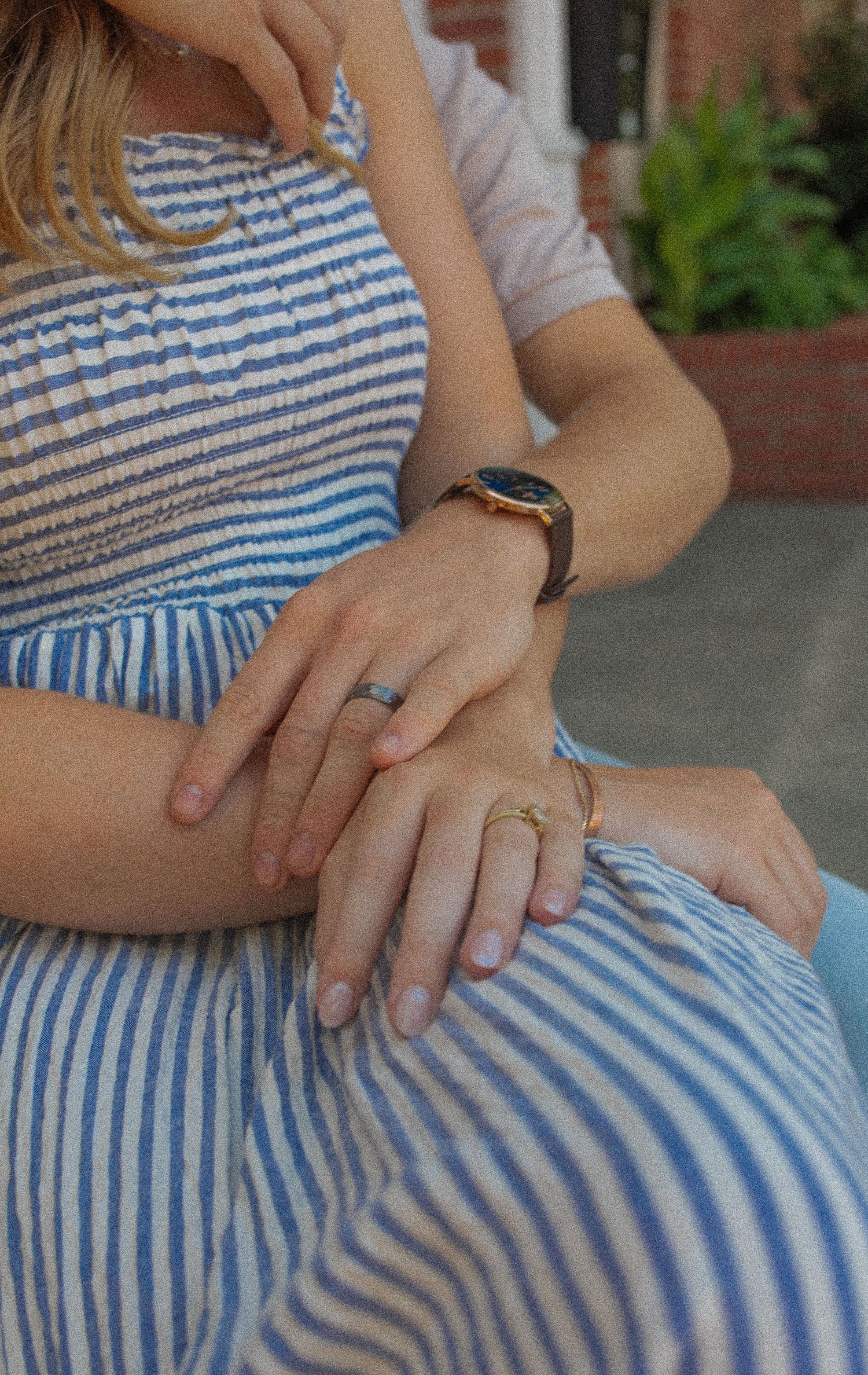 Close-up view of hands folded on lap wearing a blue and white striped summer dress with a watch and ring visible.