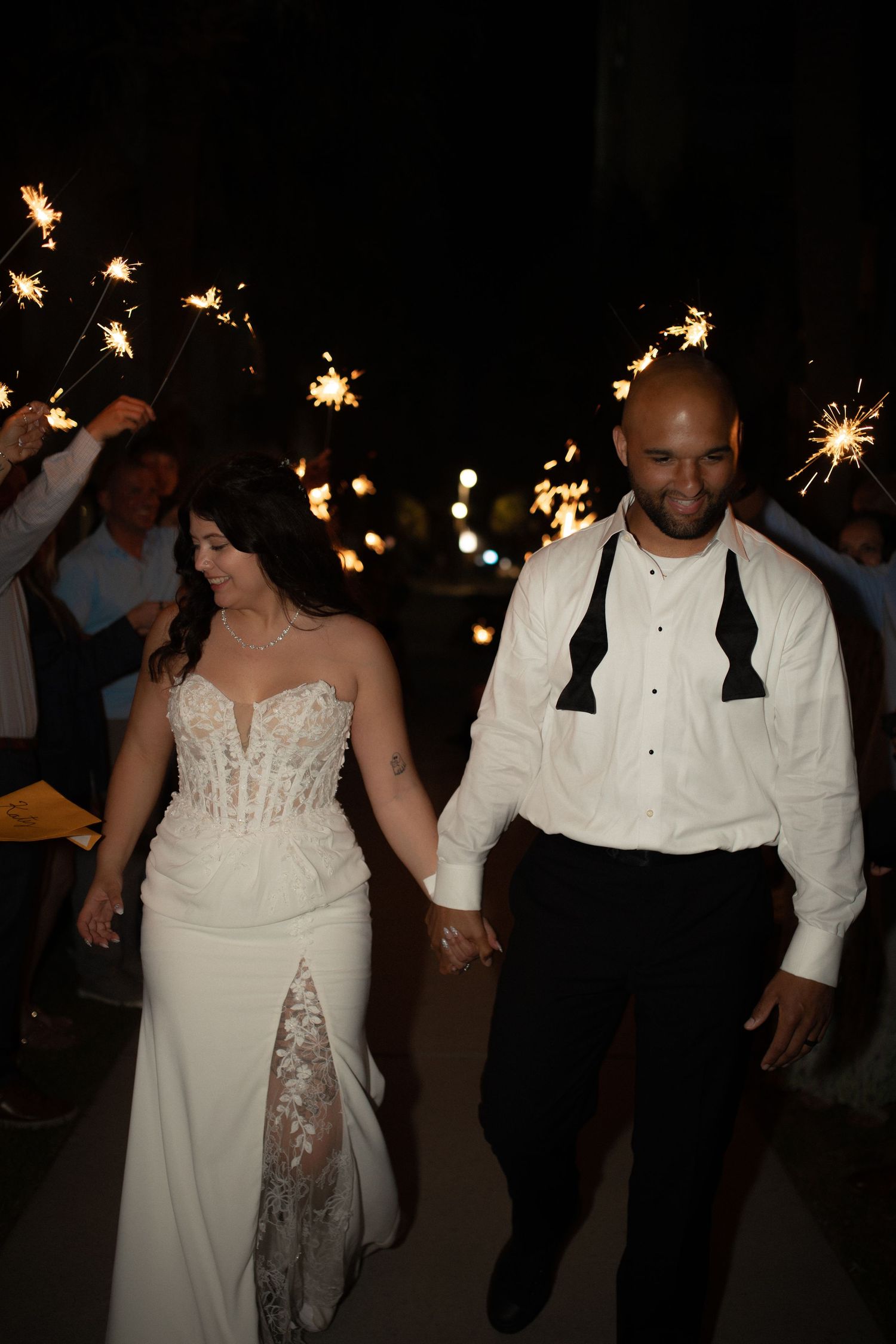 Bride and groom walk through sparkler send-off at night wedding celebration, holding hands in elegant attire.