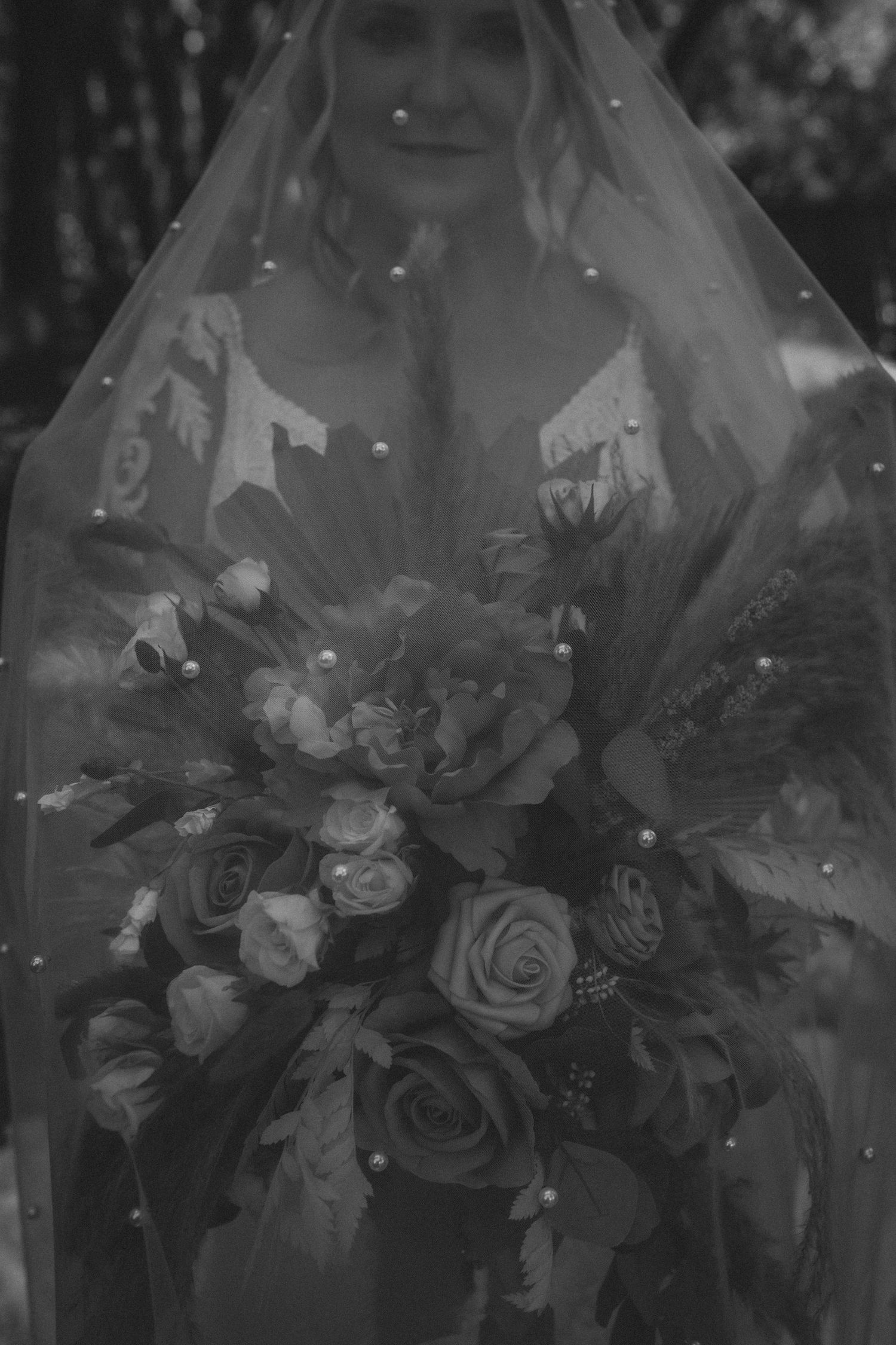A black and white wedding photo featuring a bride holding a lush bouquet of roses and mixed flowers under a veil.
