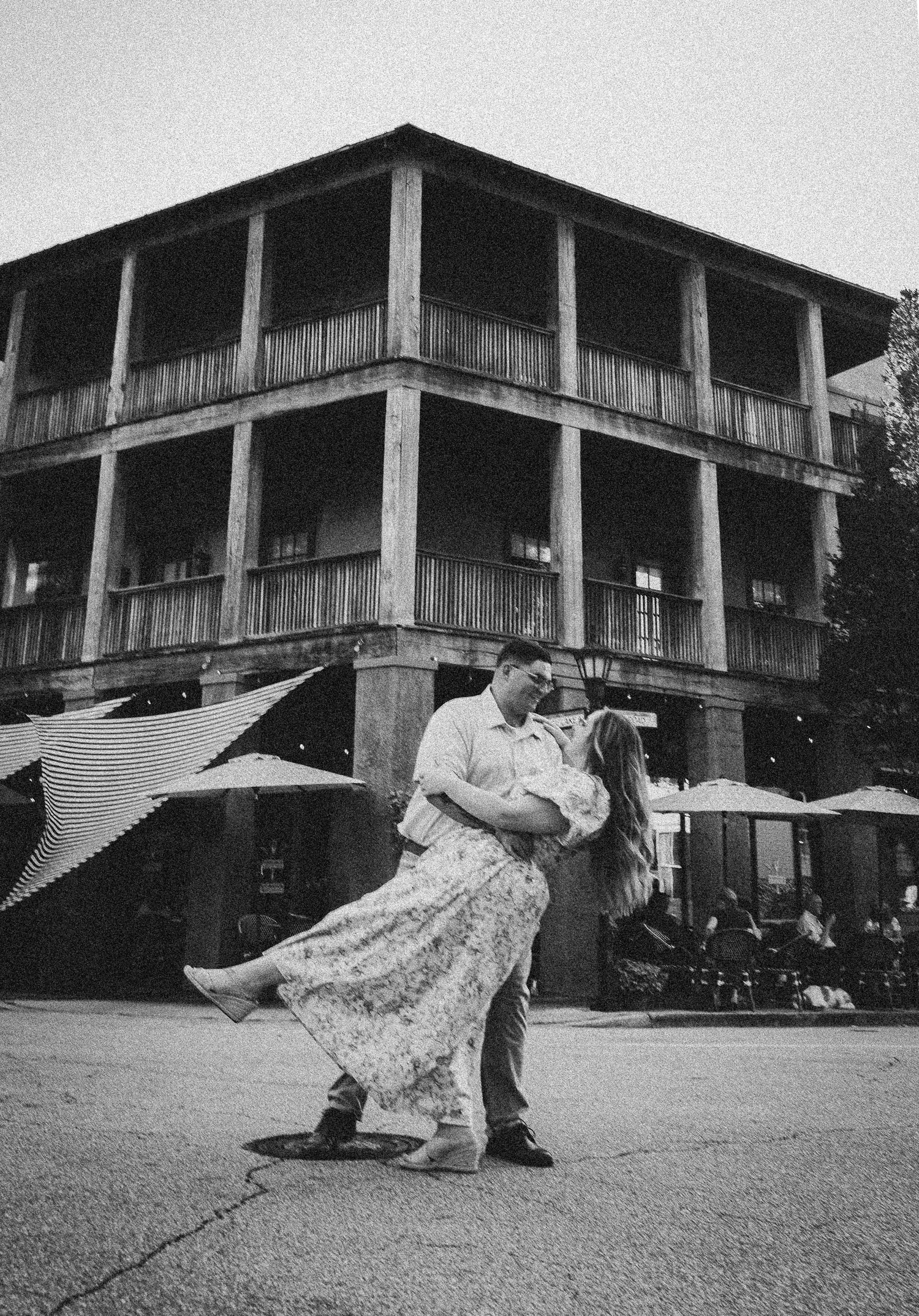 A romantic couple dancing outside a historic two-story building in black and white.