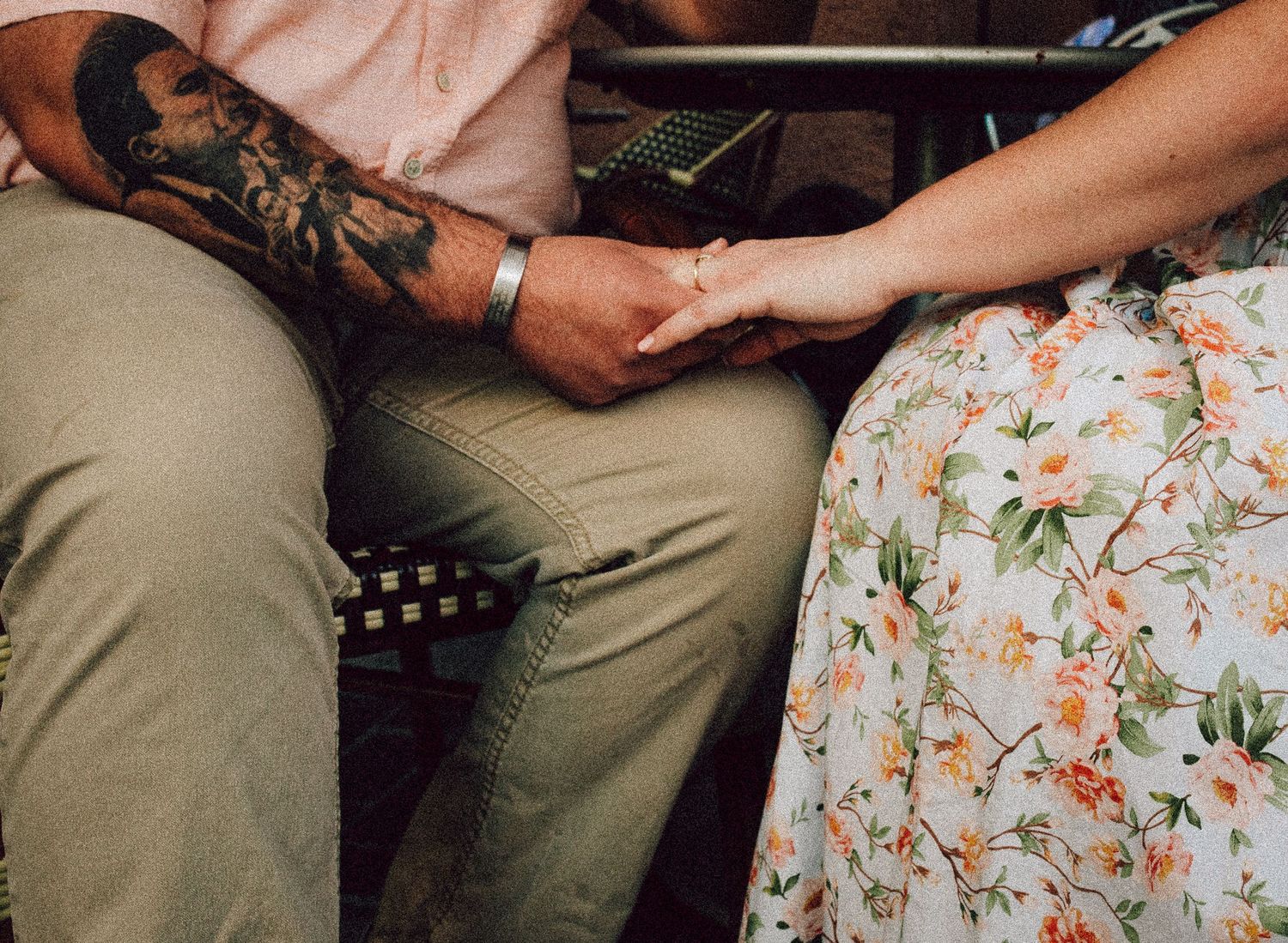 Close-up of hands holding together with visible tattoo and floral dress fabric.