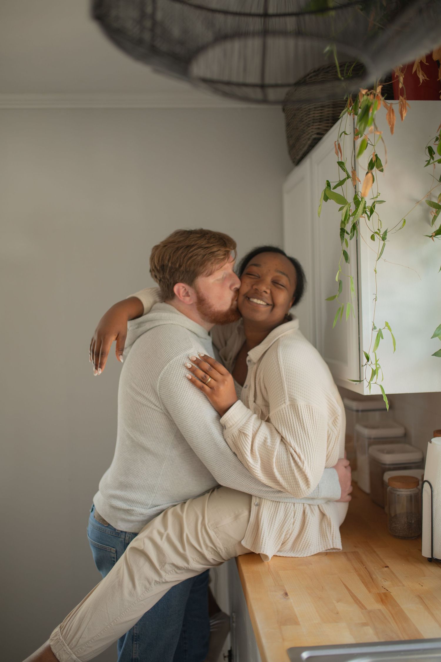 Two people in light colored clothing embrace and share a joyful moment together in a bright indoor space.