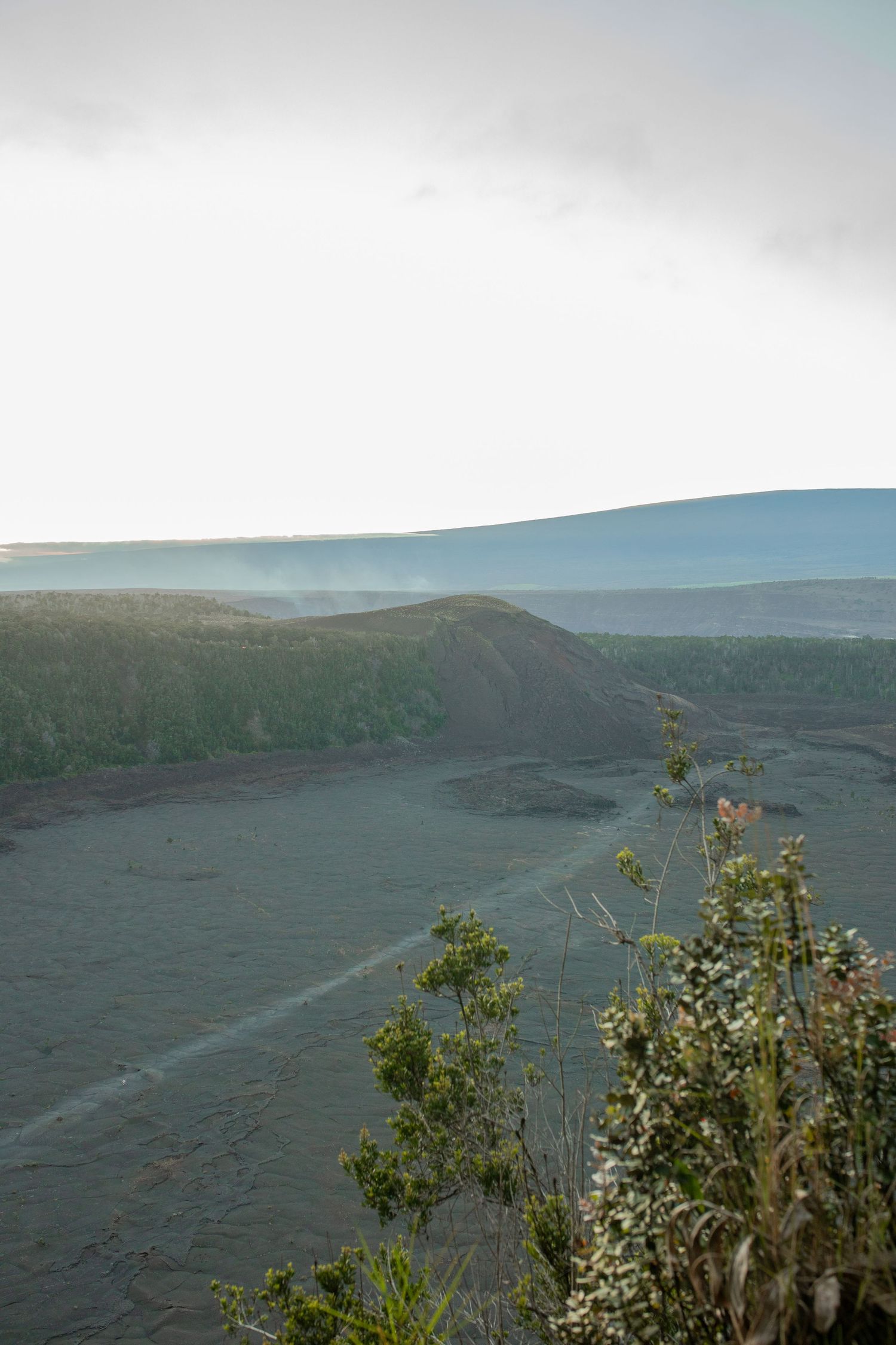 Volcanic landscape at twilight with misty hills and sparse vegetation against a pale sky at Kilauea crater in Hawaii.