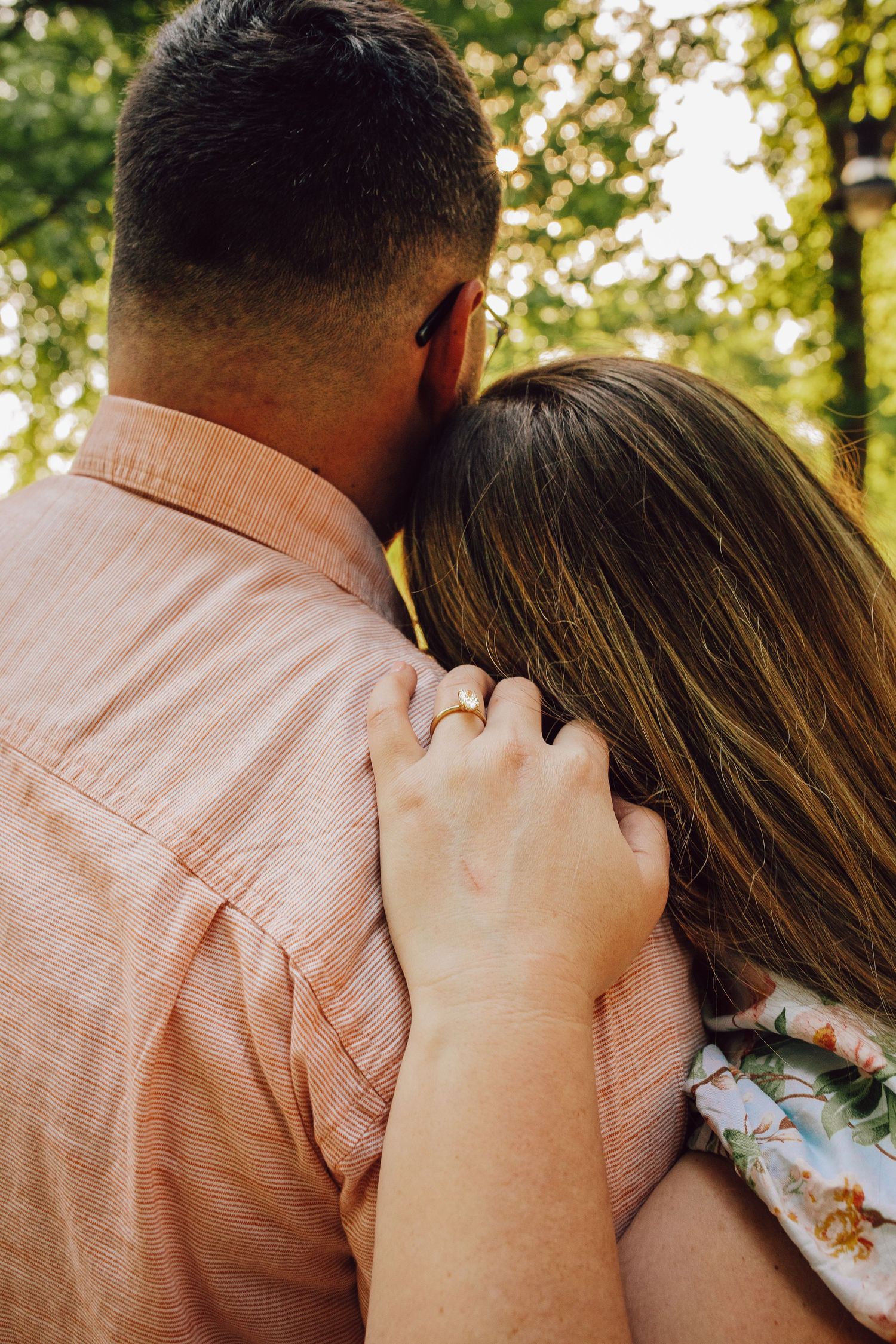 Close-up of couple embracing outdoors with sunlit trees in background.