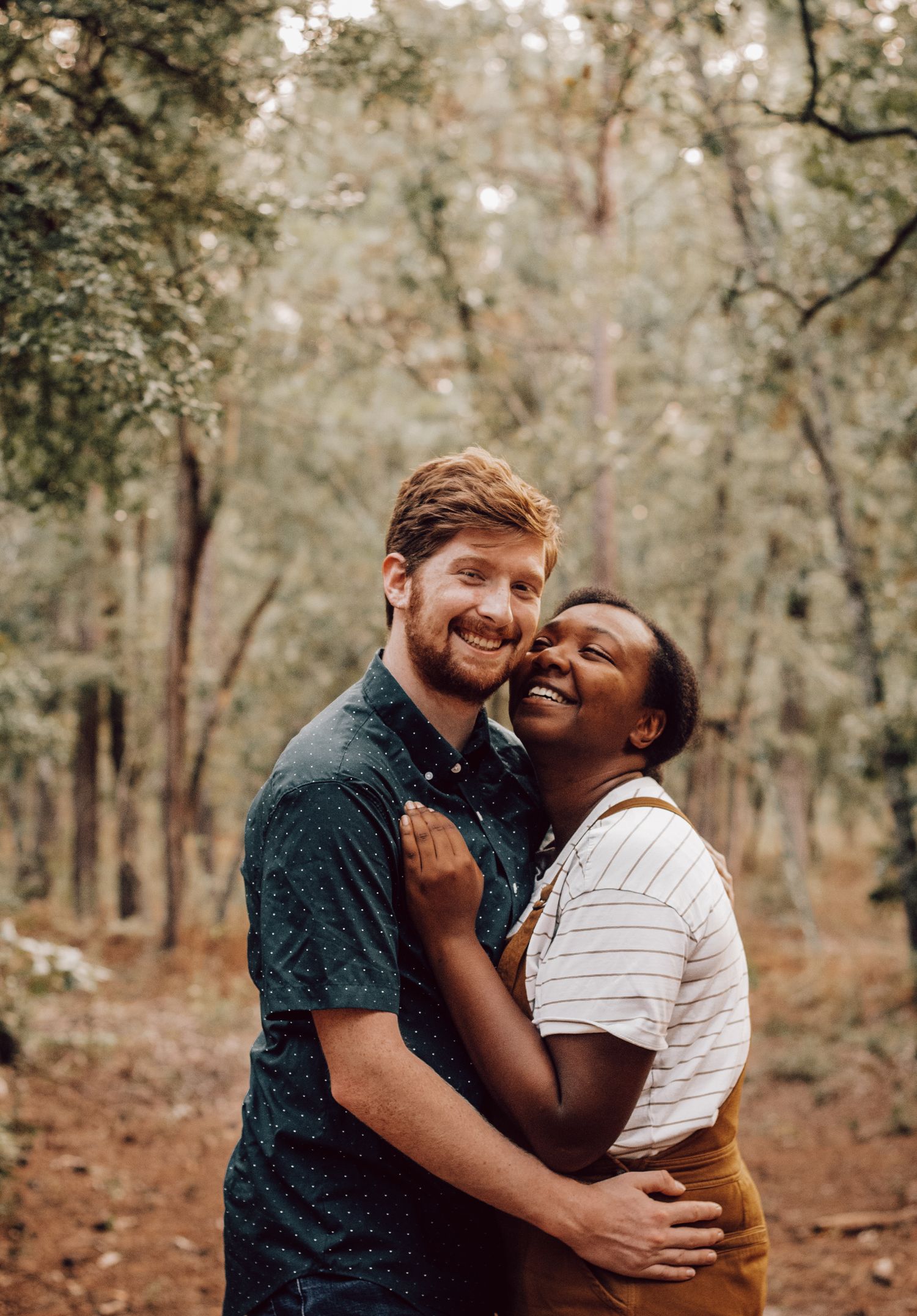 Happy couple embracing and laughing in a wooded forest setting.