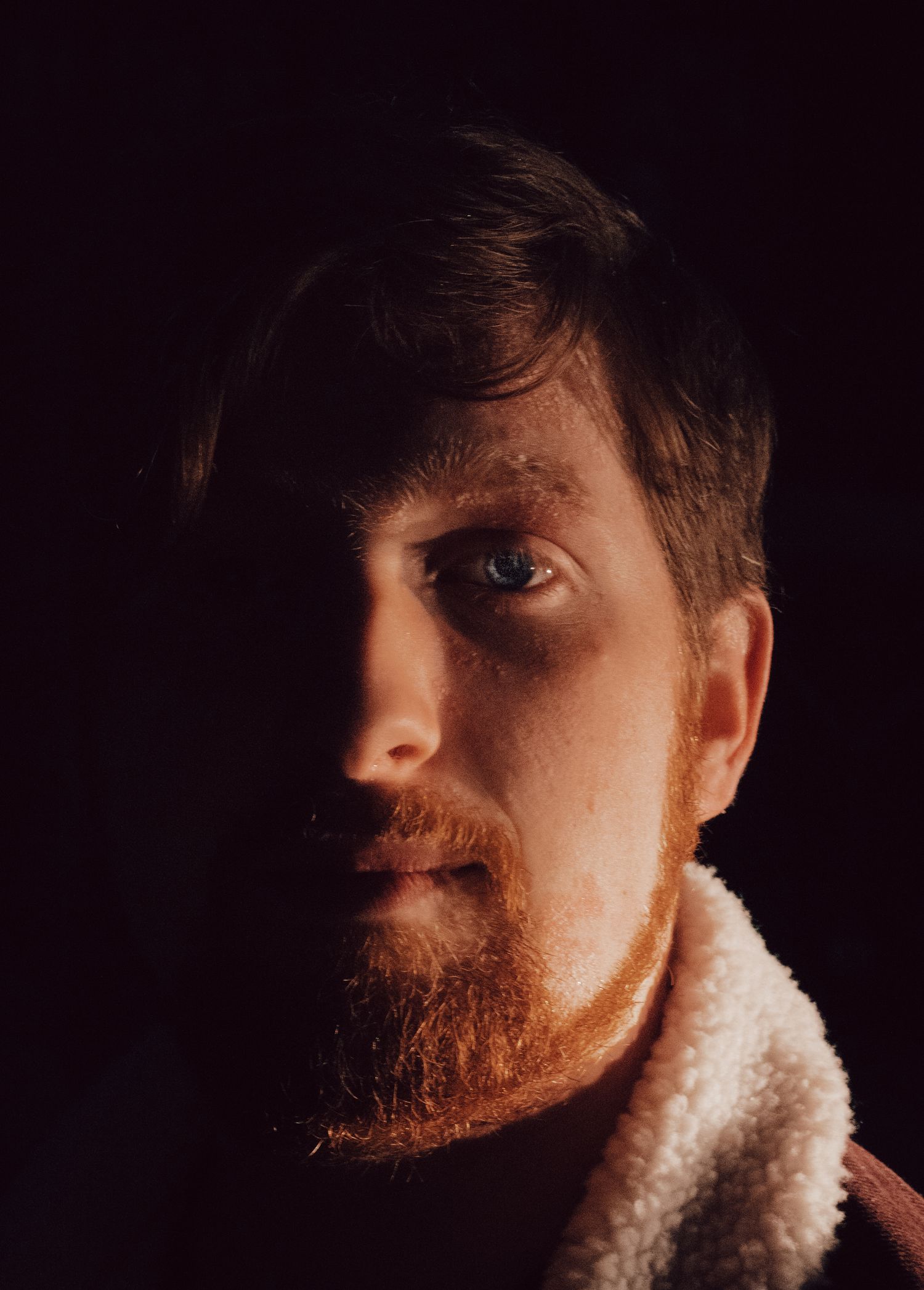 A dramatic side-lit portrait showing half a face in shadow against a dark background.