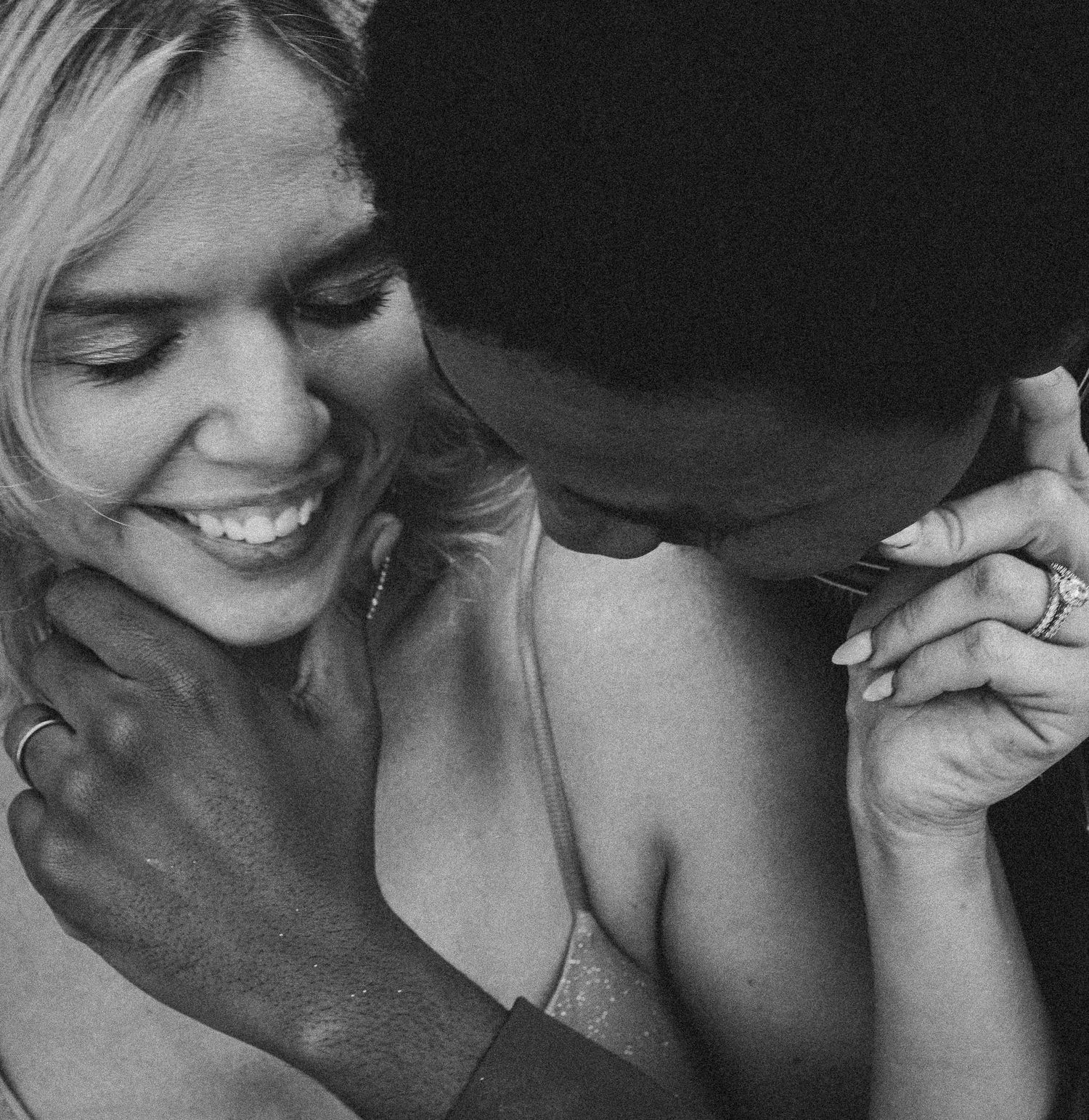 Black and white photo of a smiling couple sharing an intimate moment, woman laughing as man nuzzles her neck.