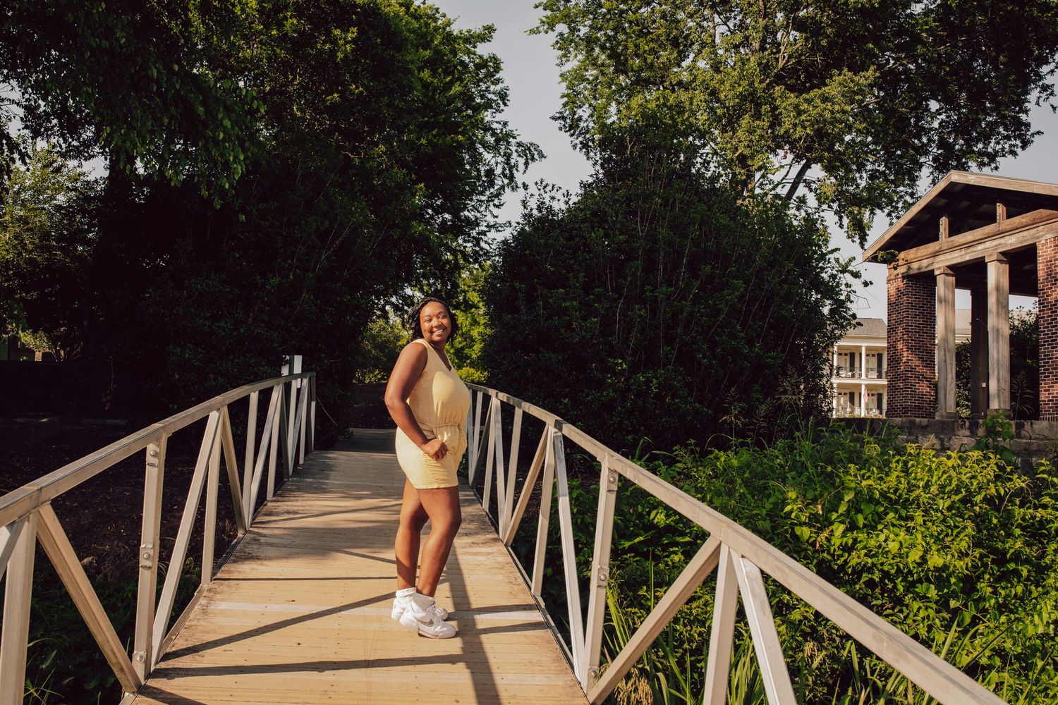 Athletic figure standing on wooden bridge walkway surrounded by greenery on sunny day.
