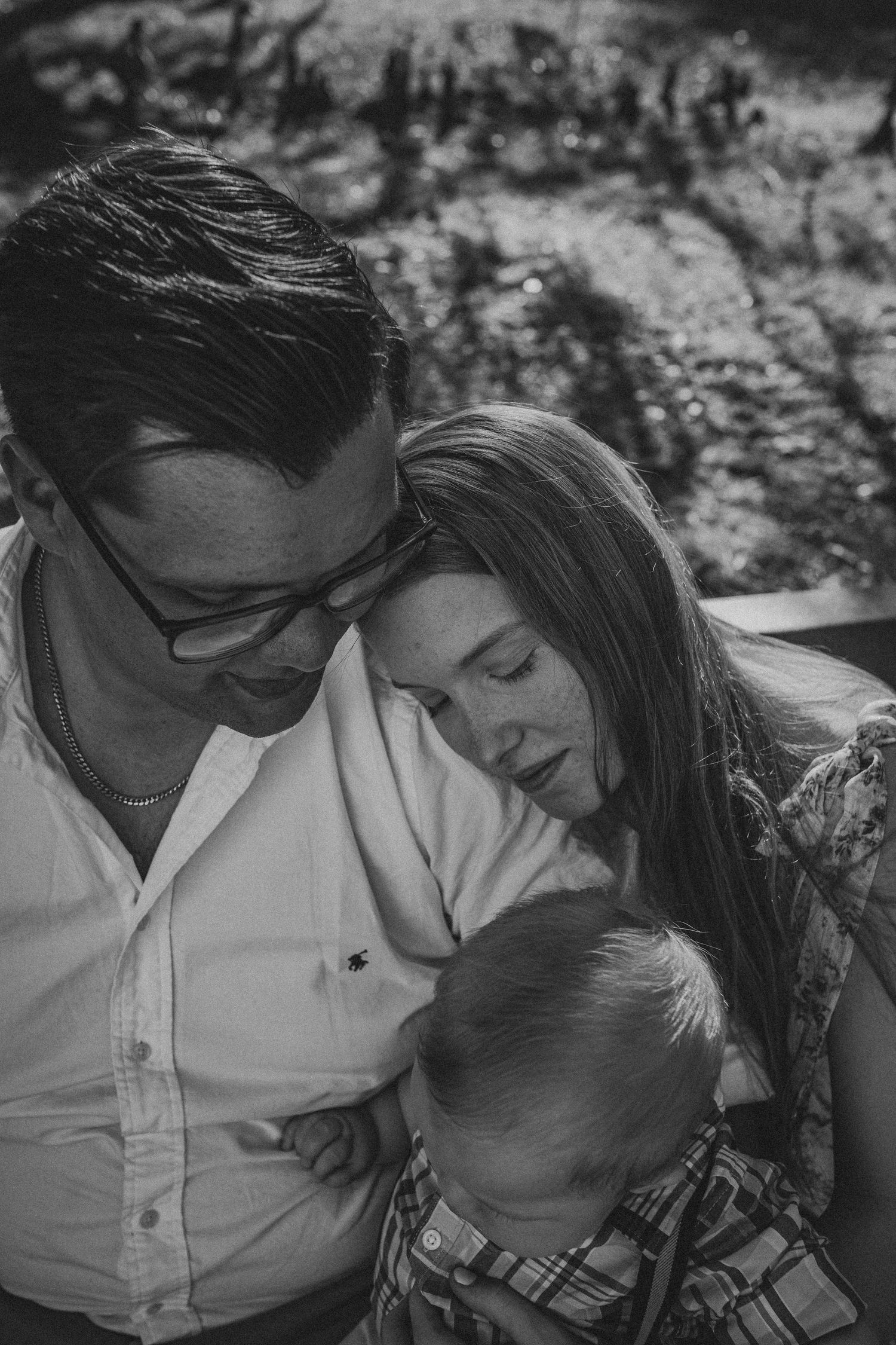 A black and white candid family portrait showing an intimate moment of closeness and connection outdoors.