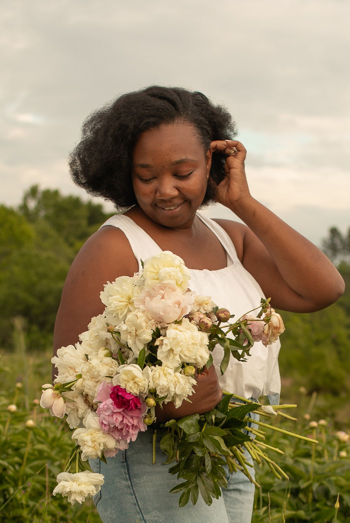 A person in a white dress holds a beautiful bouquet of pink and white flowers while standing in a lush outdoor field.
