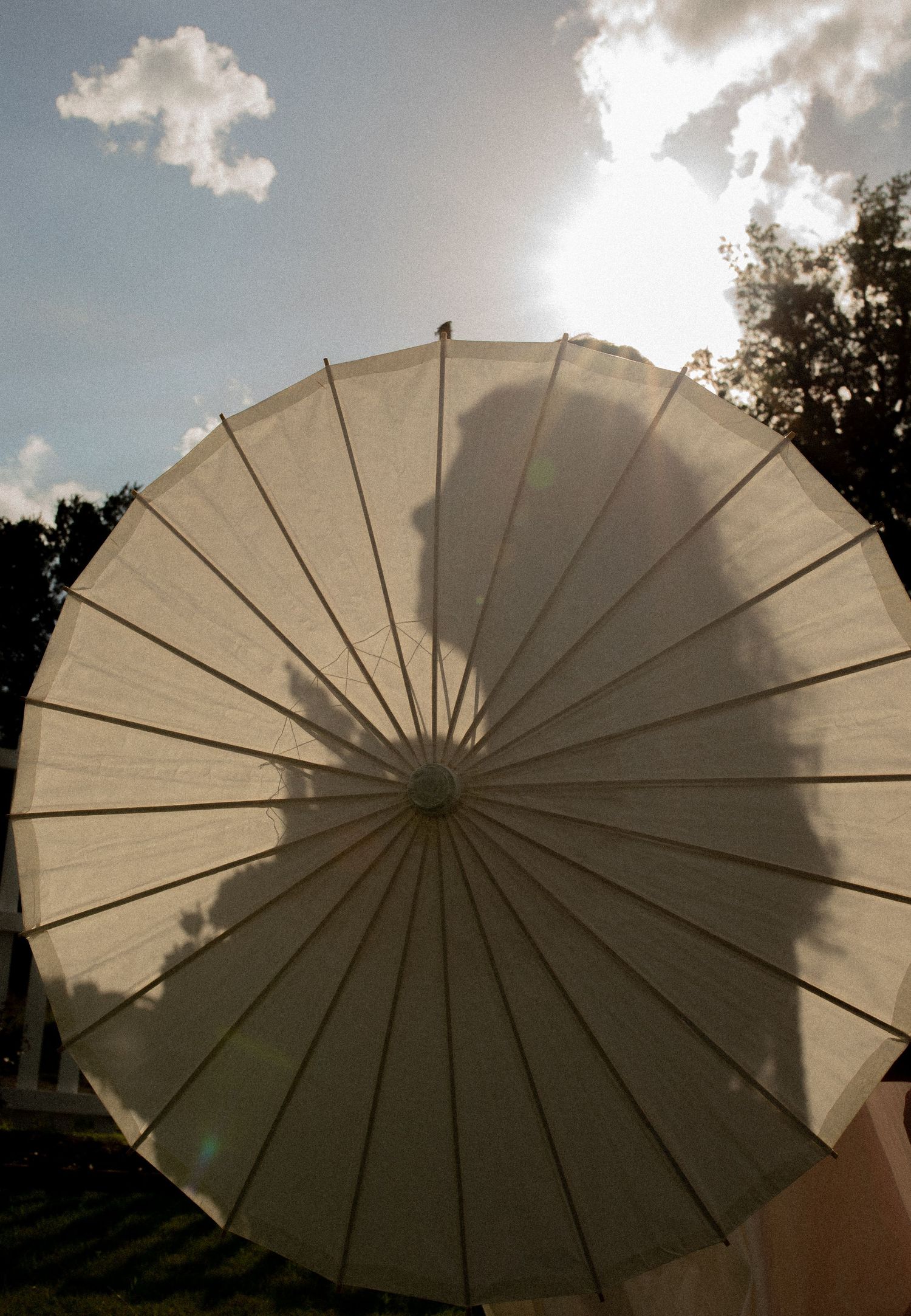Silhouette of a person visible through a white paper parasol umbrella against a bright sunny sky.