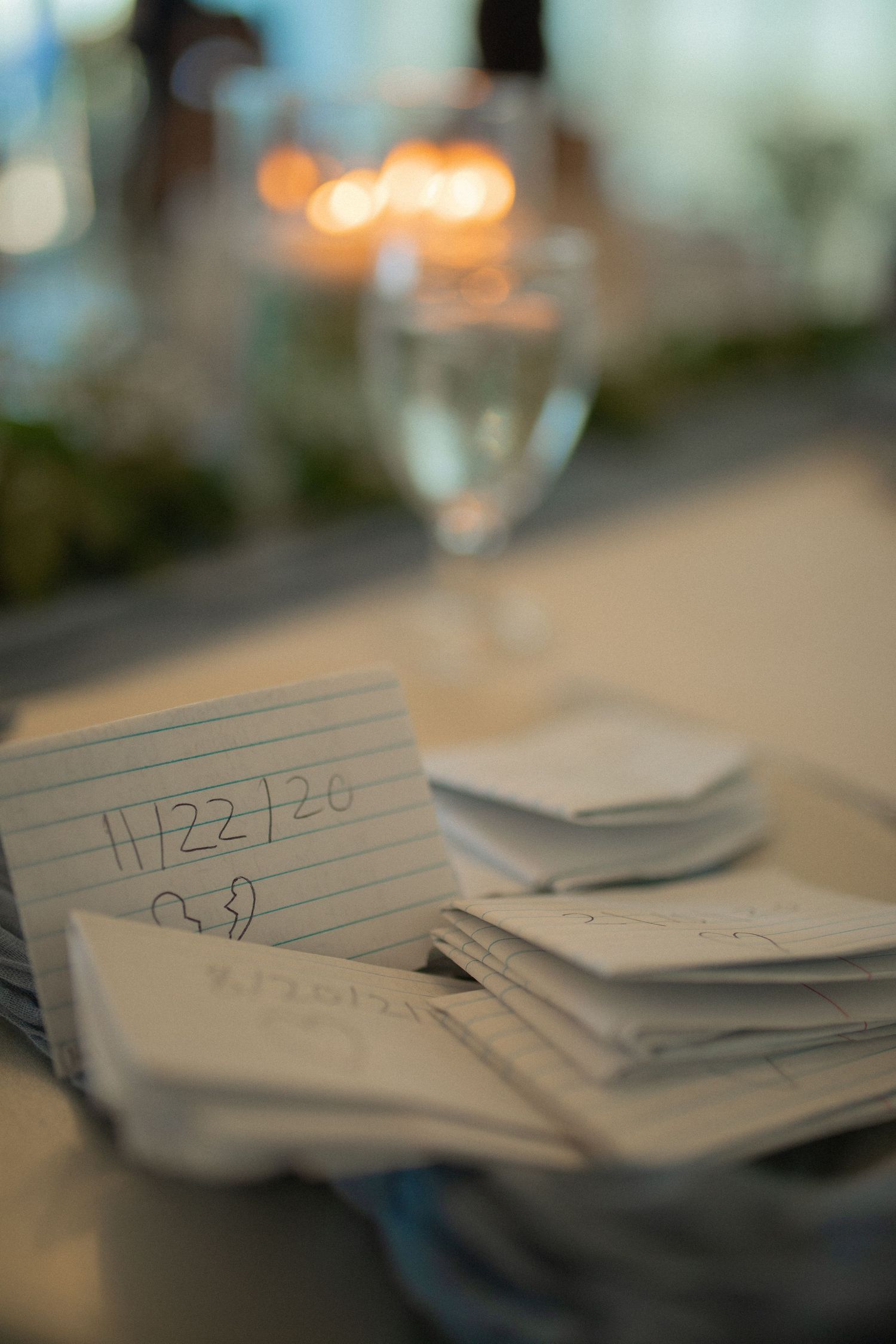 Index cards with date 11/22/20 written on them stacked on a wedding reception table with glassware.