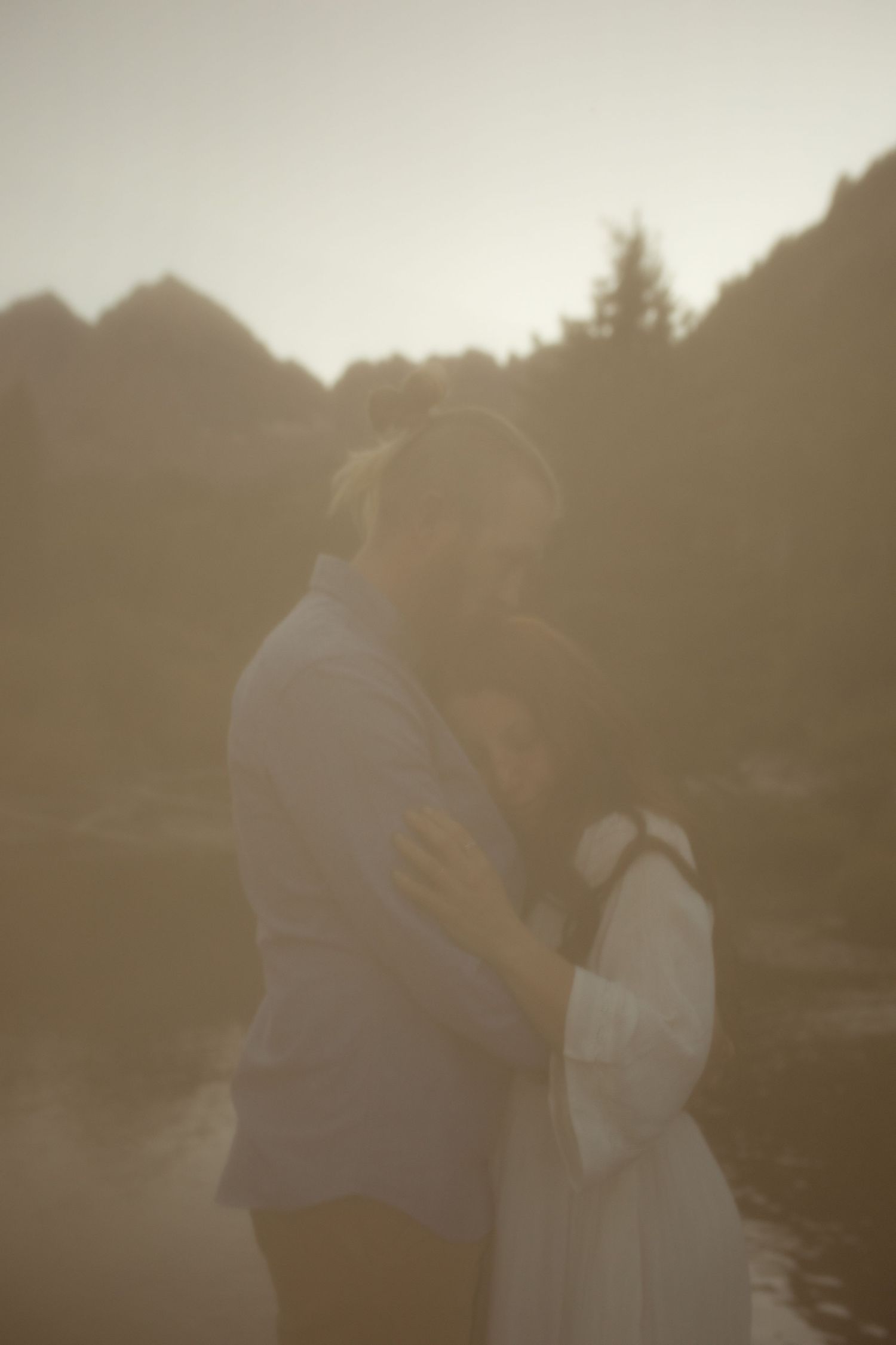 Couple embracing tenderly at golden hour with misty mountain landscape in soft warm light.
