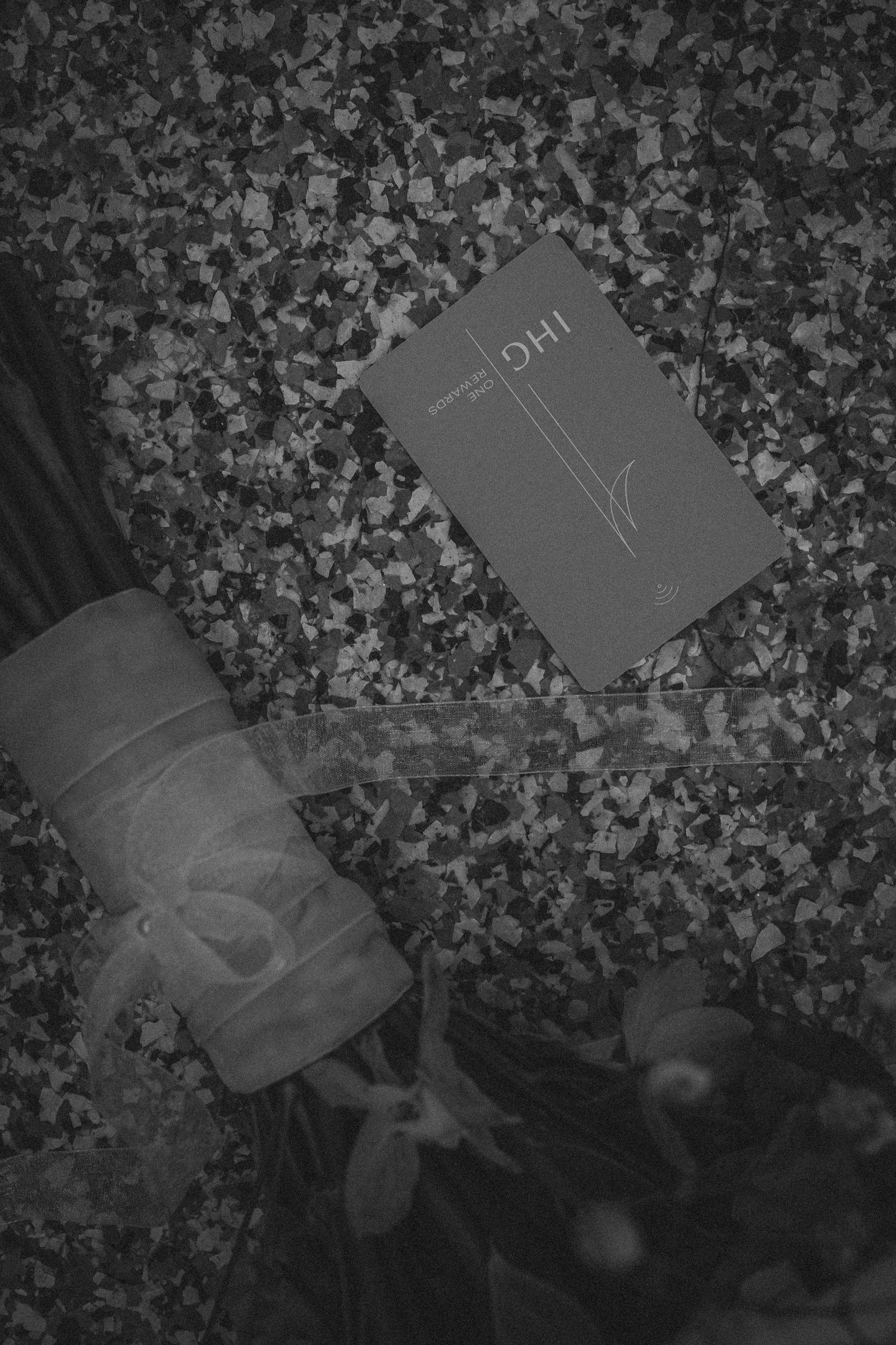 Black and white flatlay of an IHG hotel keycard and toiletry bag on a speckled surface.