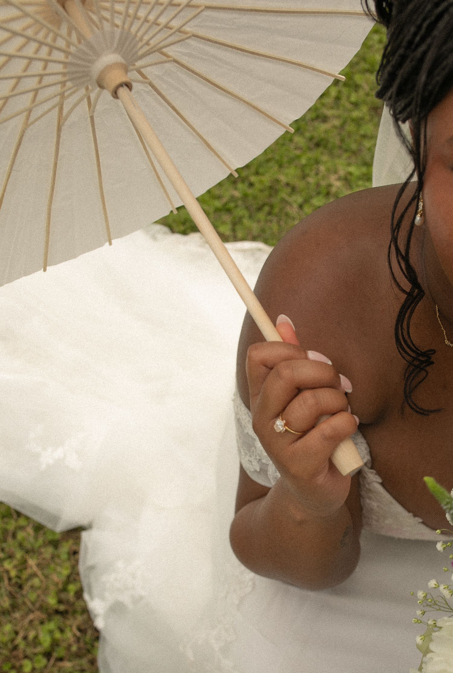 Close-up of bride in white lace gown holding a white parasol umbrella with manicured nails and ring.
