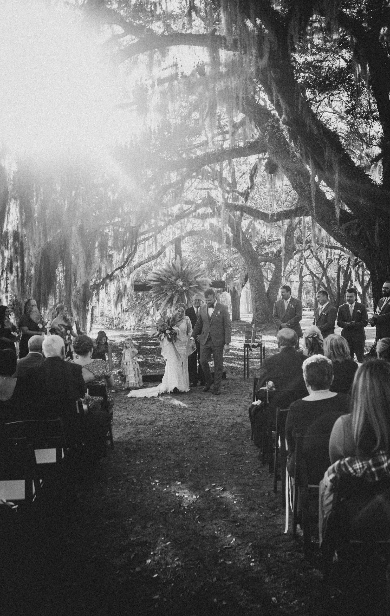 A dreamy outdoor wedding ceremony under Spanish moss-draped oak trees in black and white photography.