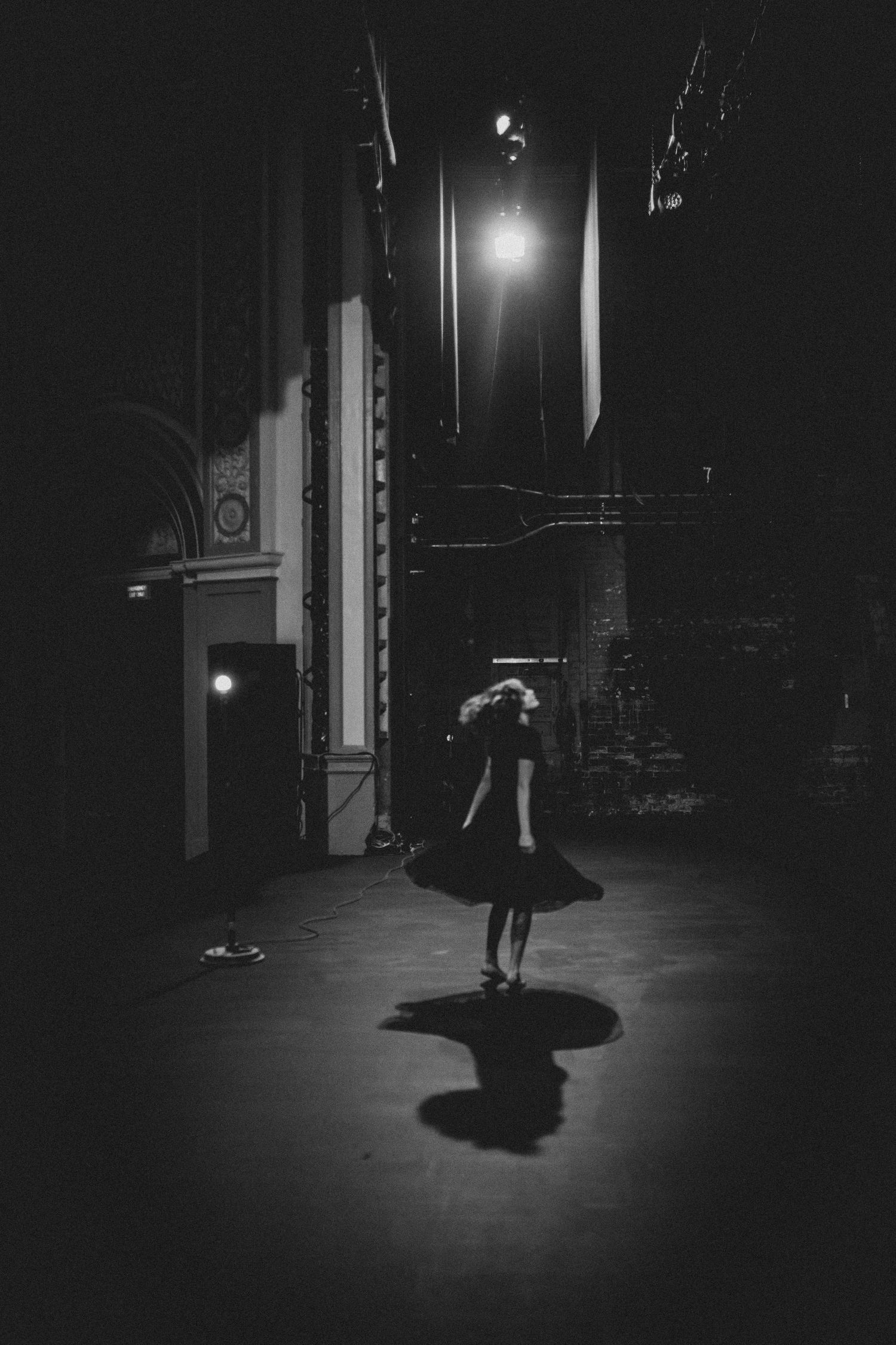 Silhouette of a dancer in a dark theater space with dramatic spotlight creating moody atmosphere.
