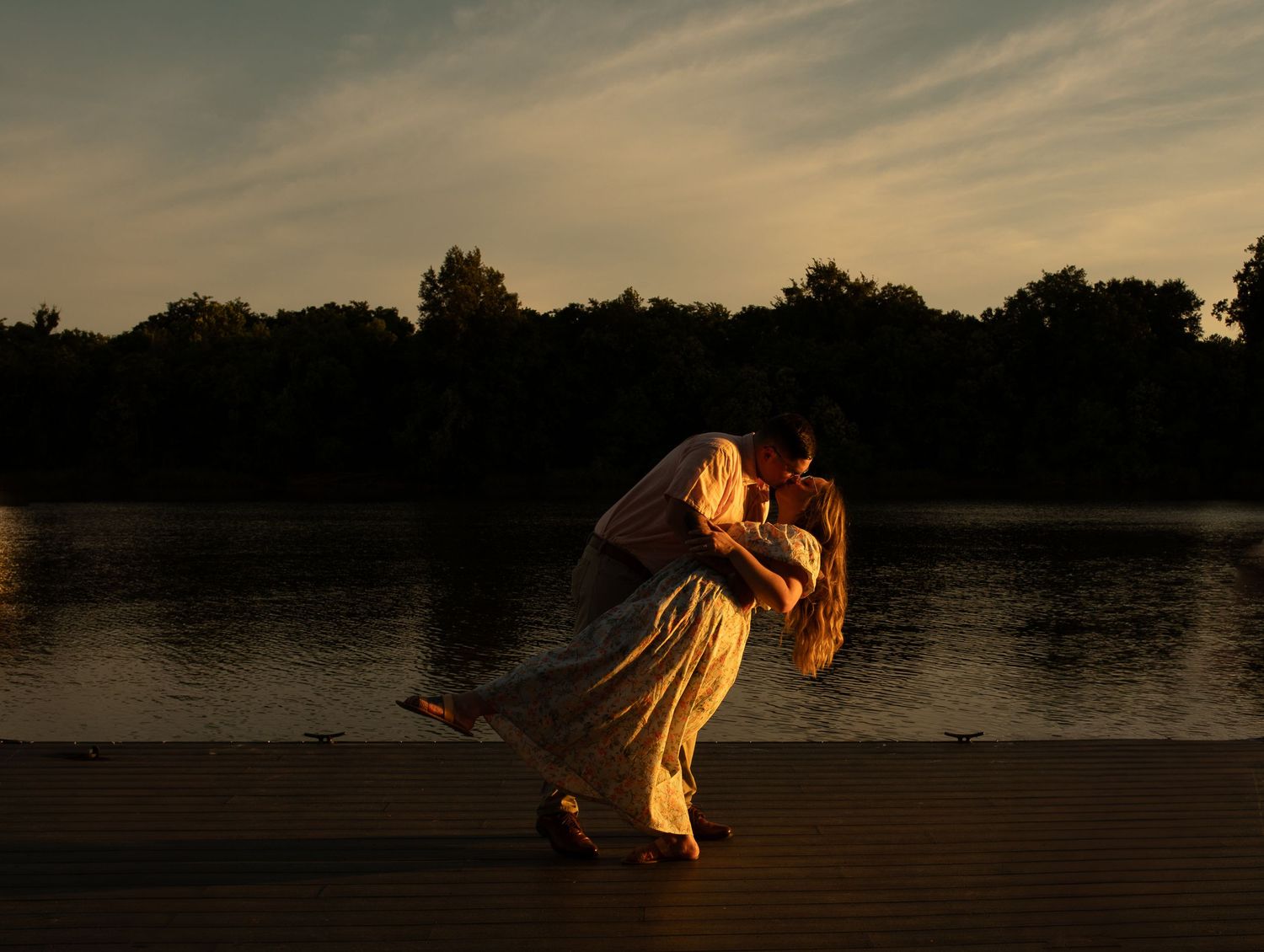 A dramatic sunset silhouette of a dancing figure on a lakeside dock.