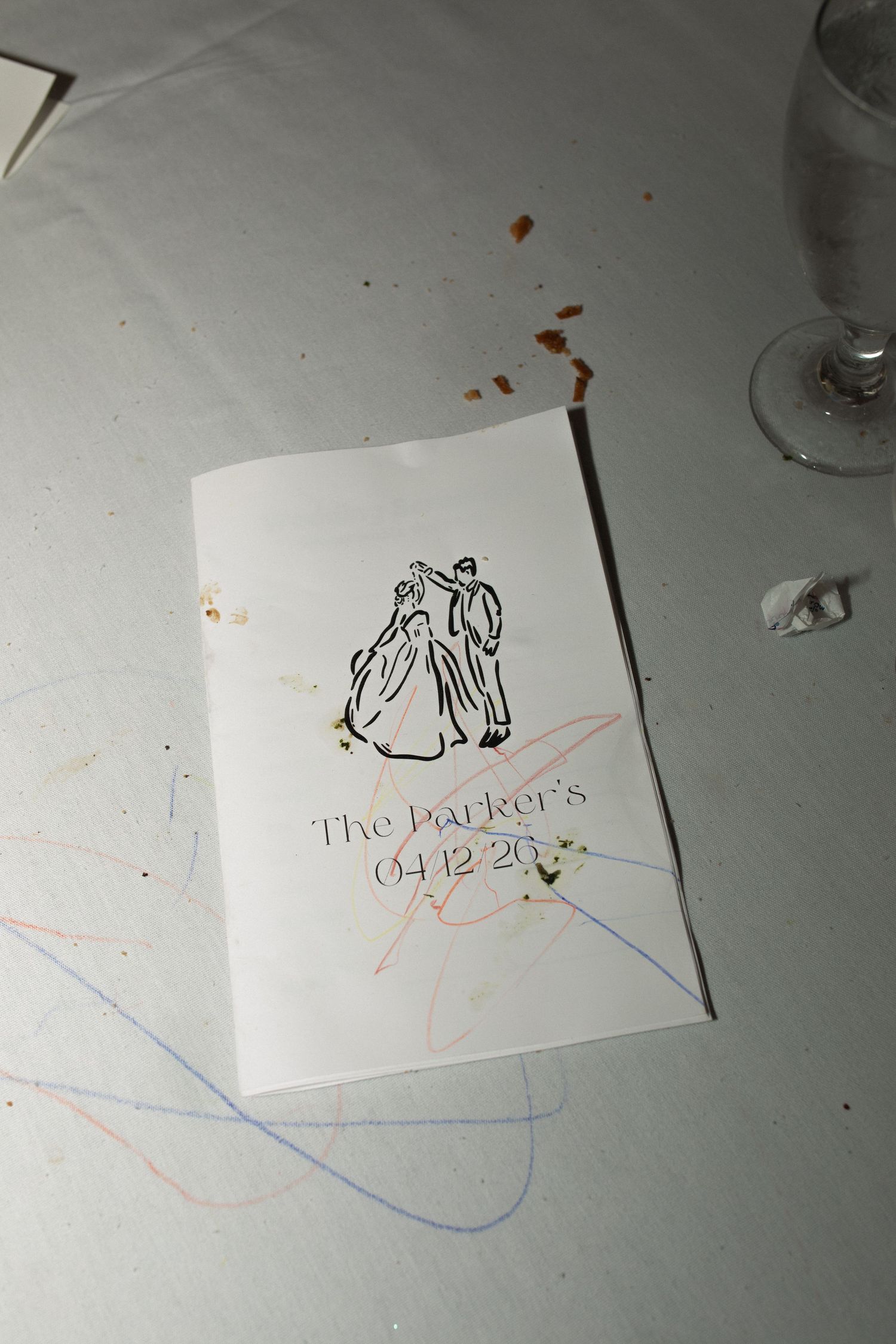 Wedding program booklet for The Parker's dated 04.12.26, featuring a dancing couple illustration, on a decorated table.