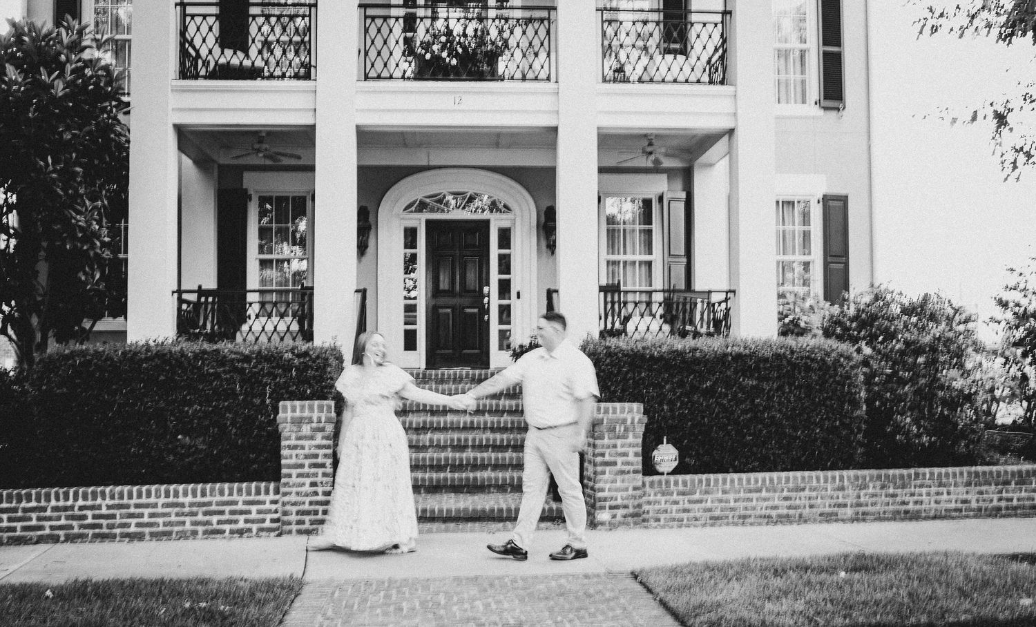 A vintage black and white photo of a stately southern mansion with people on the front steps.