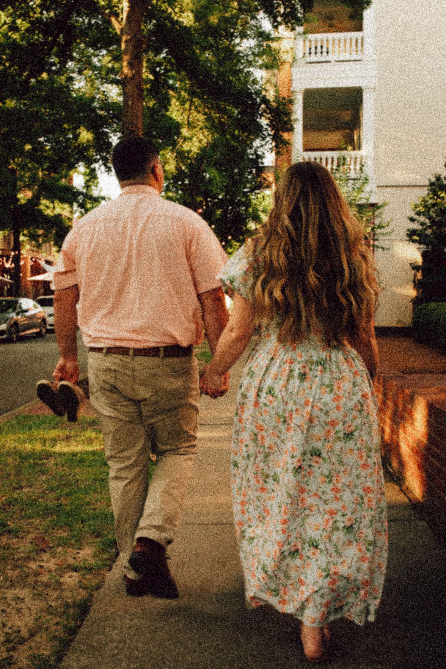 A couple holding hands while walking down a sidewalk in matching pink and floral outfits.