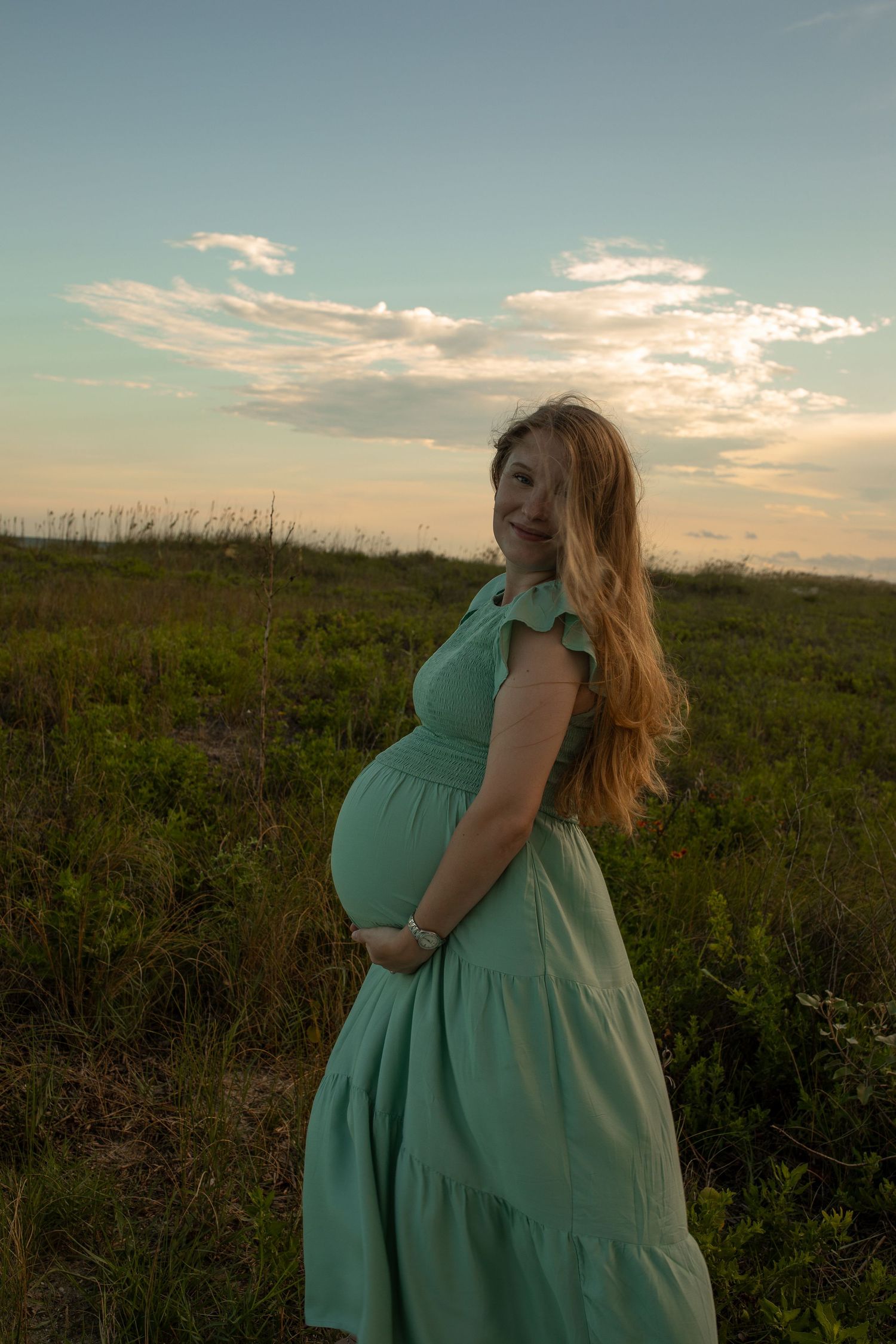 A mint green dress flows in the breeze against a sunset sky and grassy field.