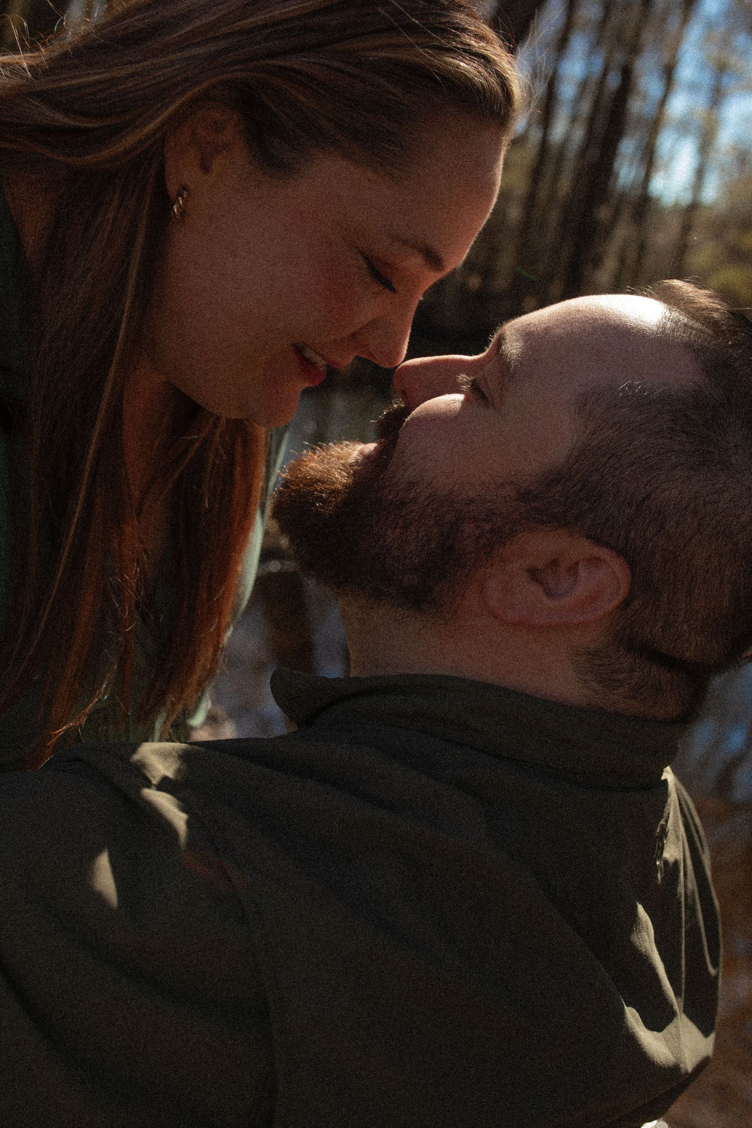 A couple shares an intimate moment together in a wooded outdoor setting during golden hour lighting.