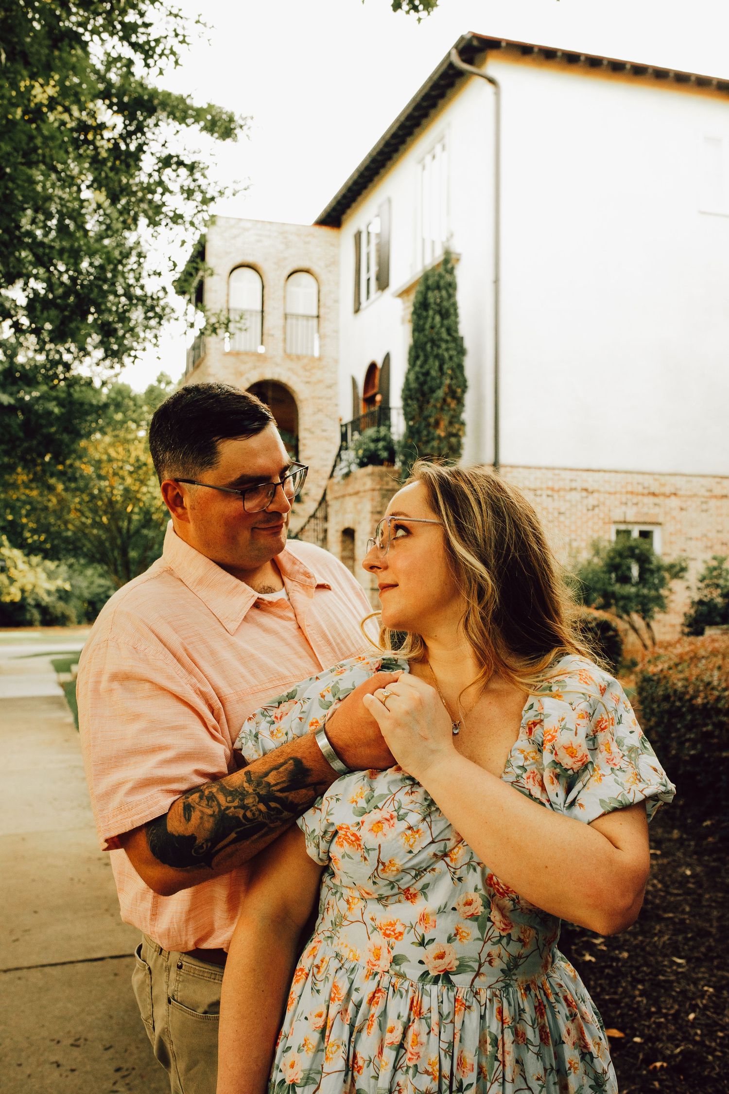 A couple shares an intimate moment outside a Mediterranean-style building with arched windows.