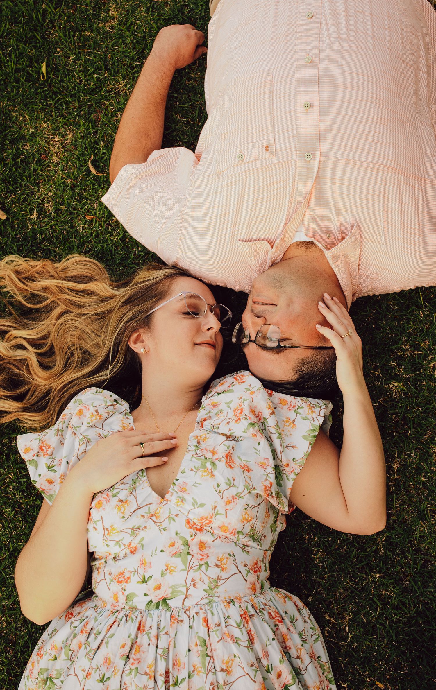 A romantic overhead shot of a couple lying on grass with their heads together.