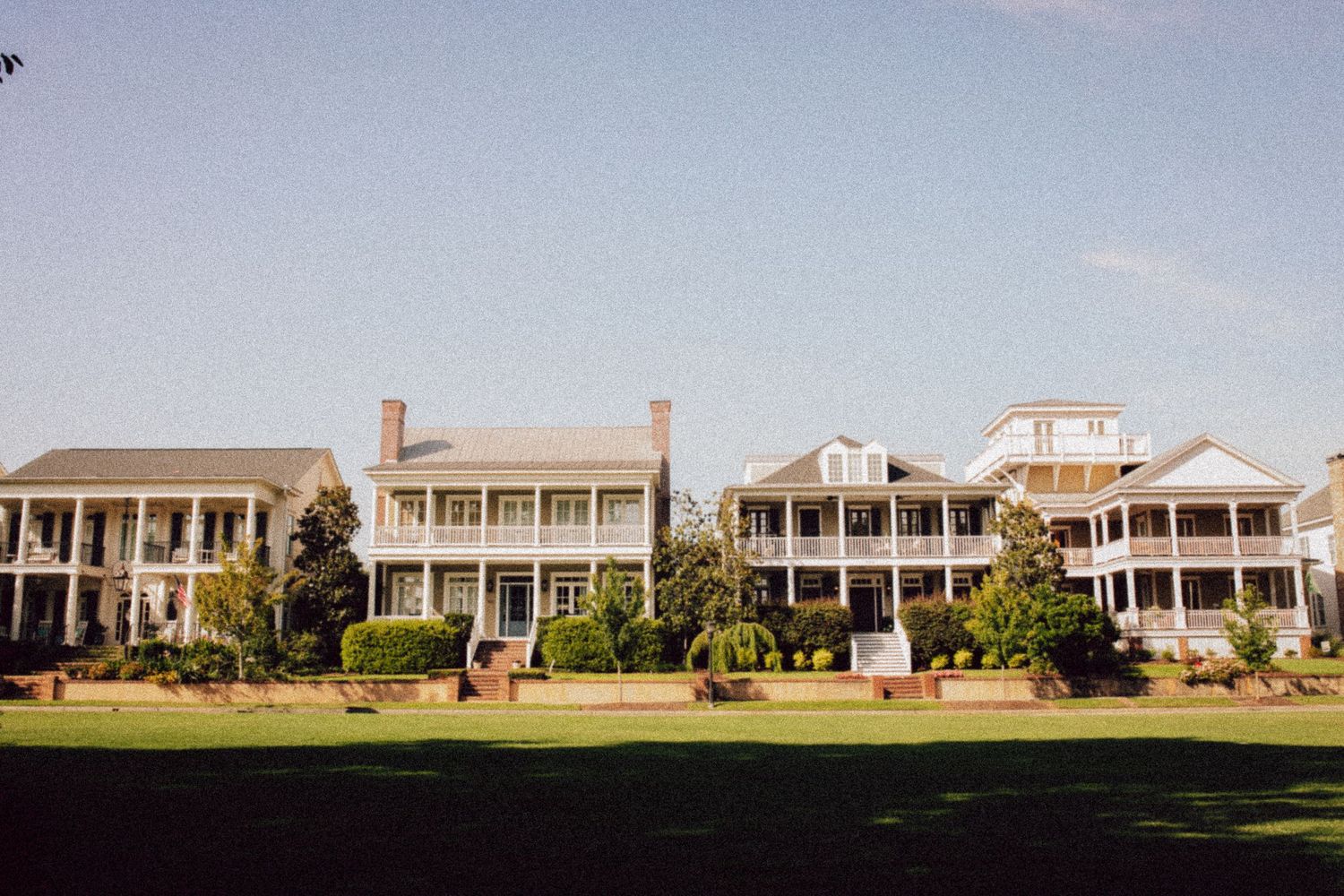 A row of stately southern colonial mansions with grand white columns and wraparound porches.