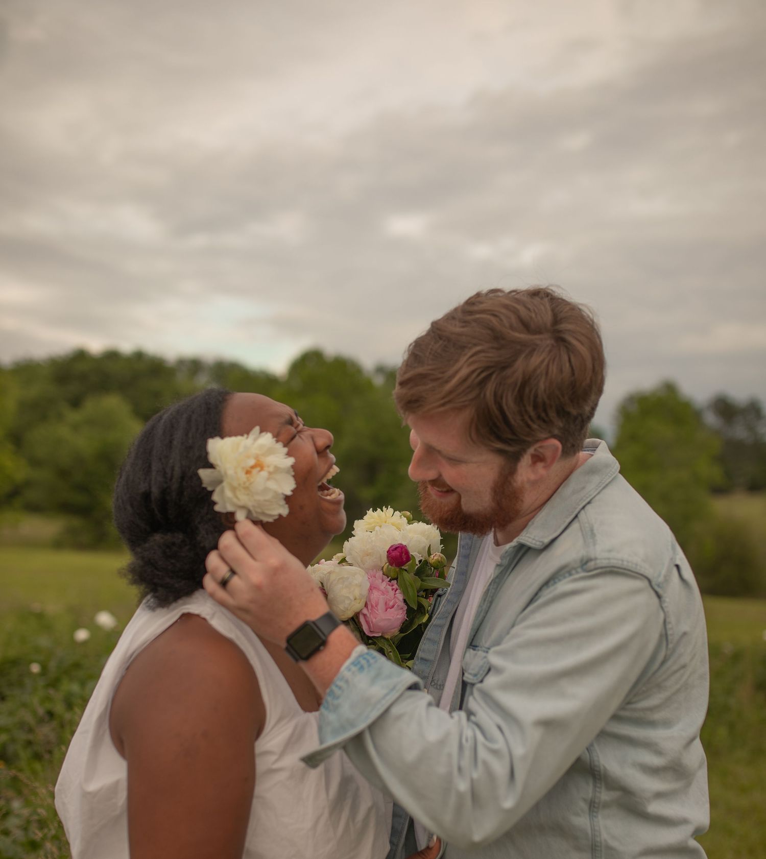 A couple shares a tender kiss in a field on a cloudy day.