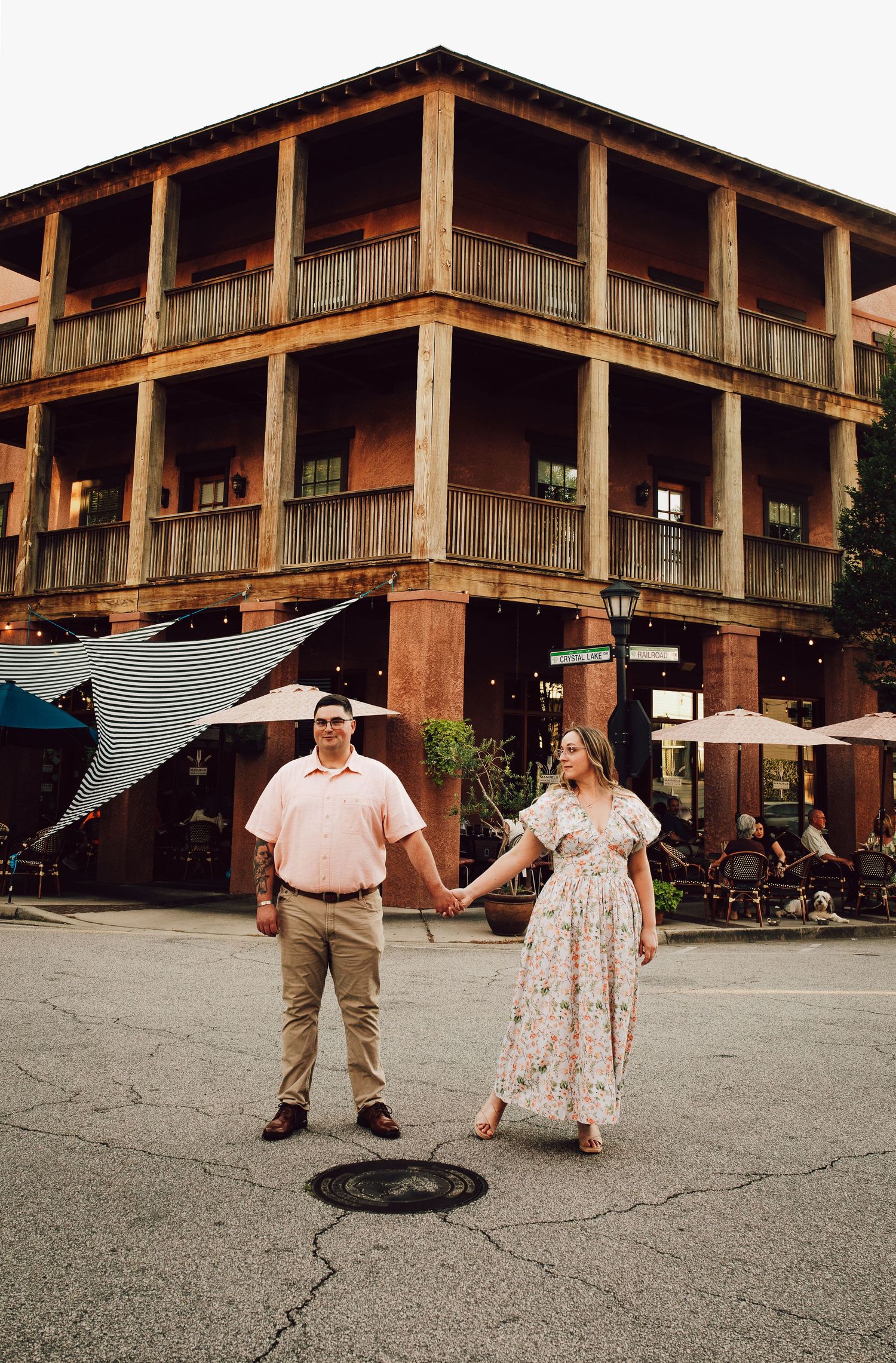 A couple posing playfully in front of a rustic three-story building with wooden balconies.