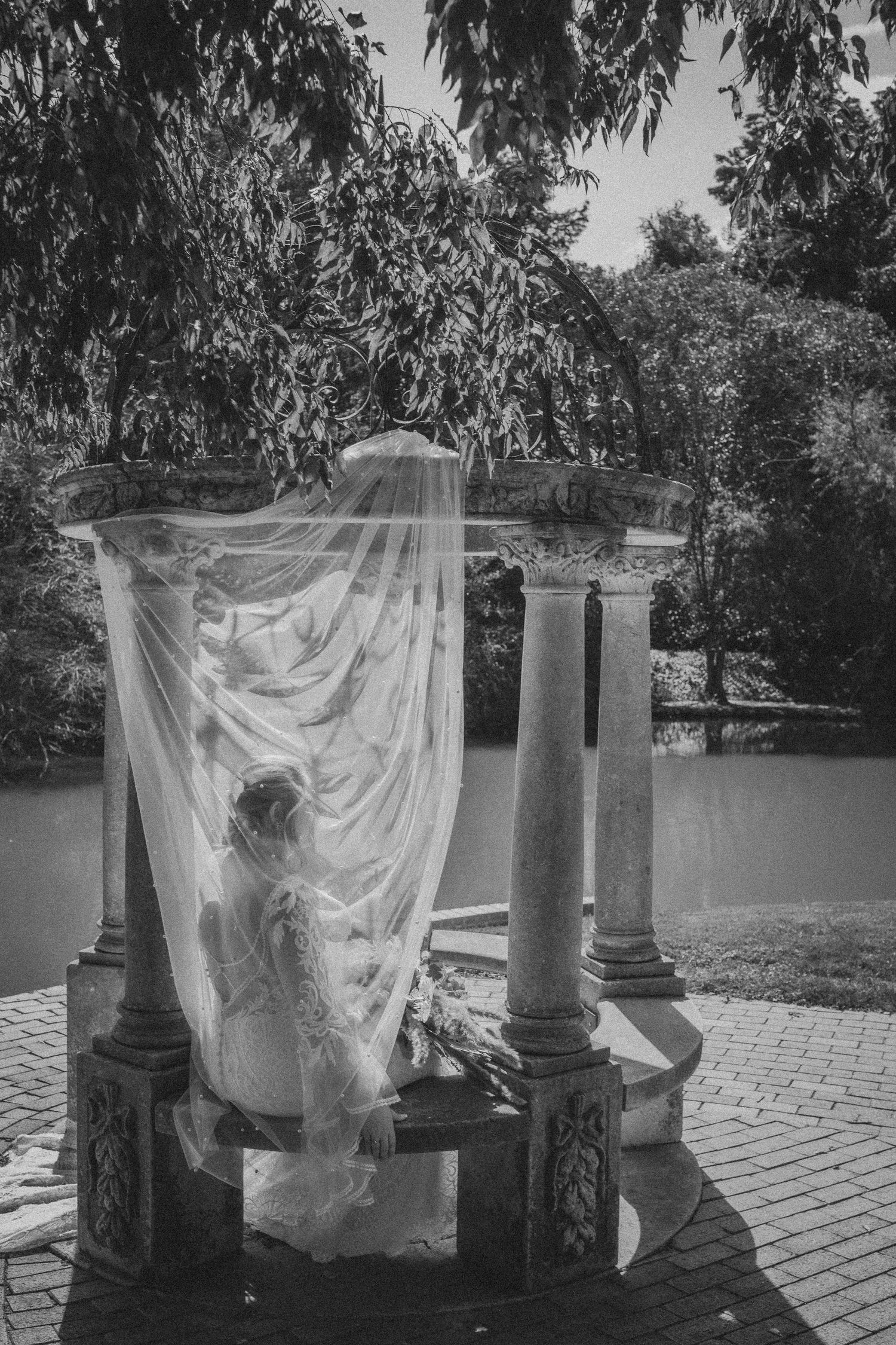 A flowing white veil billows between classical pillars in a dreamy black and white outdoor garden setting.