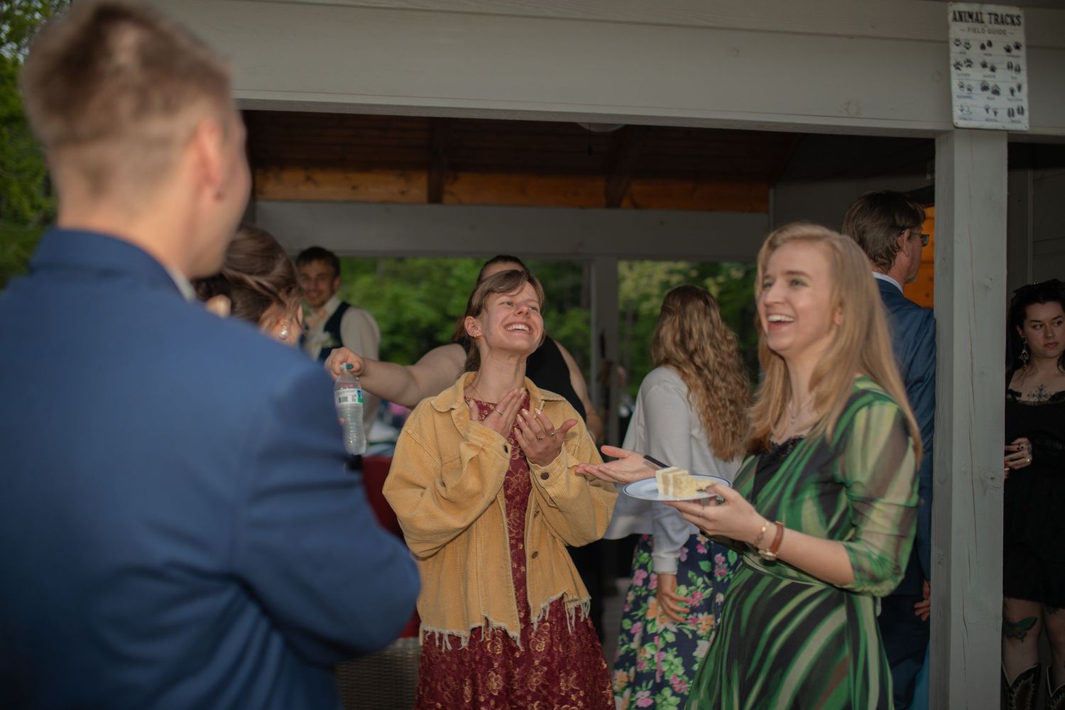 Guests laughing and socializing at an outdoor wedding reception near a pavilion in the evening.