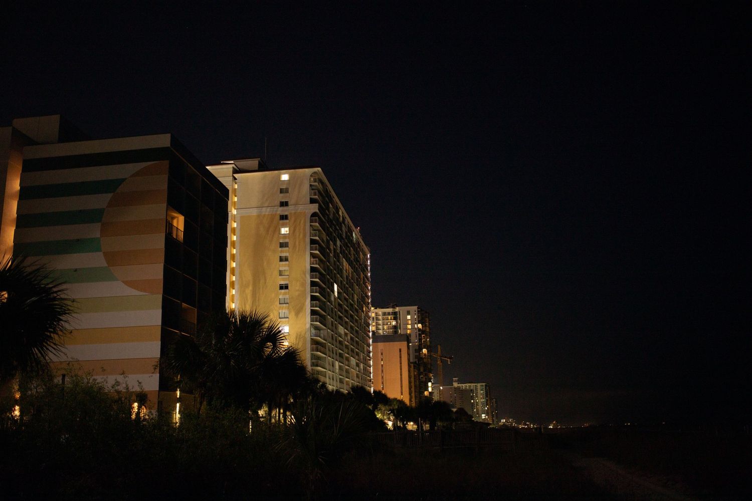 Tall beachfront hotel buildings illuminated at night with palm trees silhouetted against a dark sky.