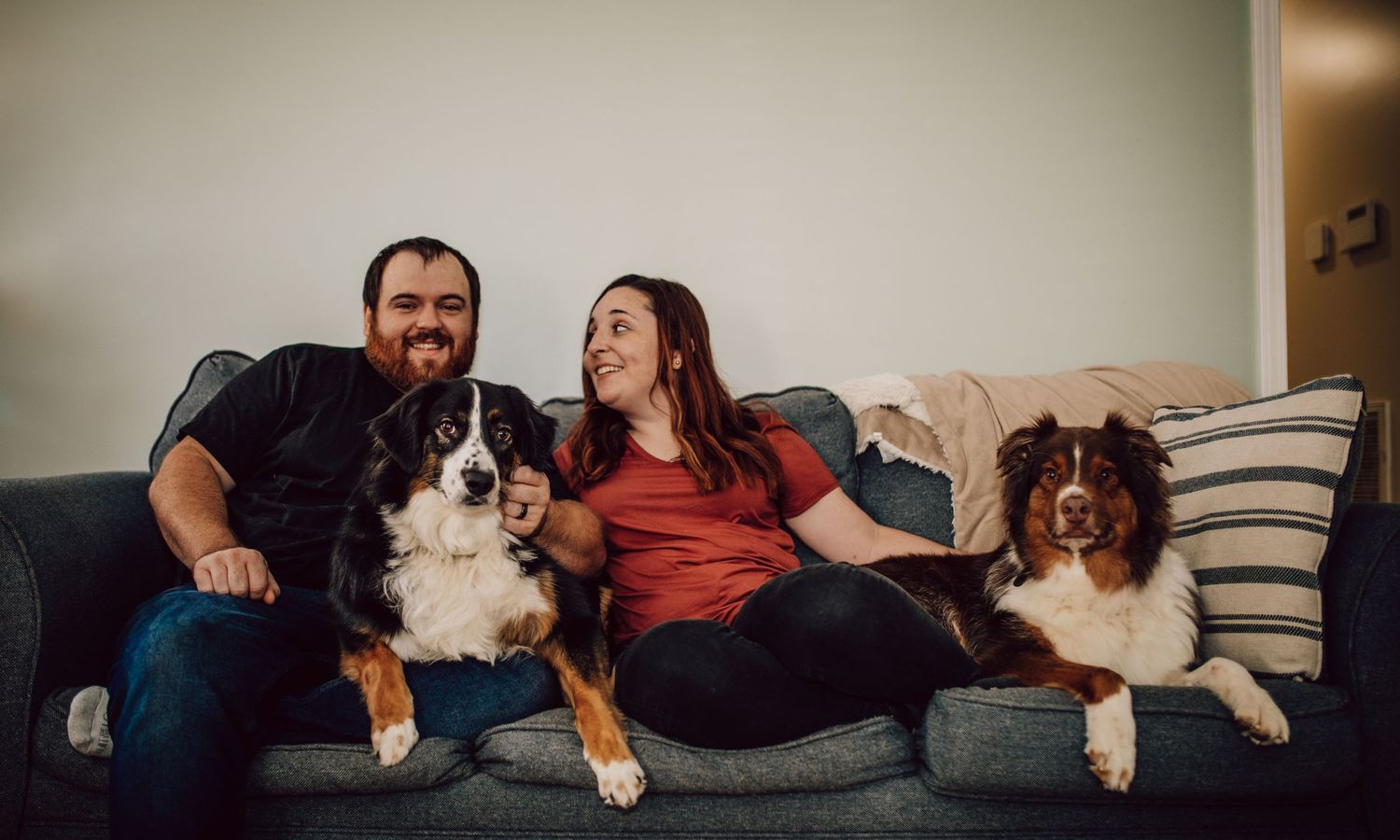 Casual family photo on grey couch with two dogs in a bright living room setting.