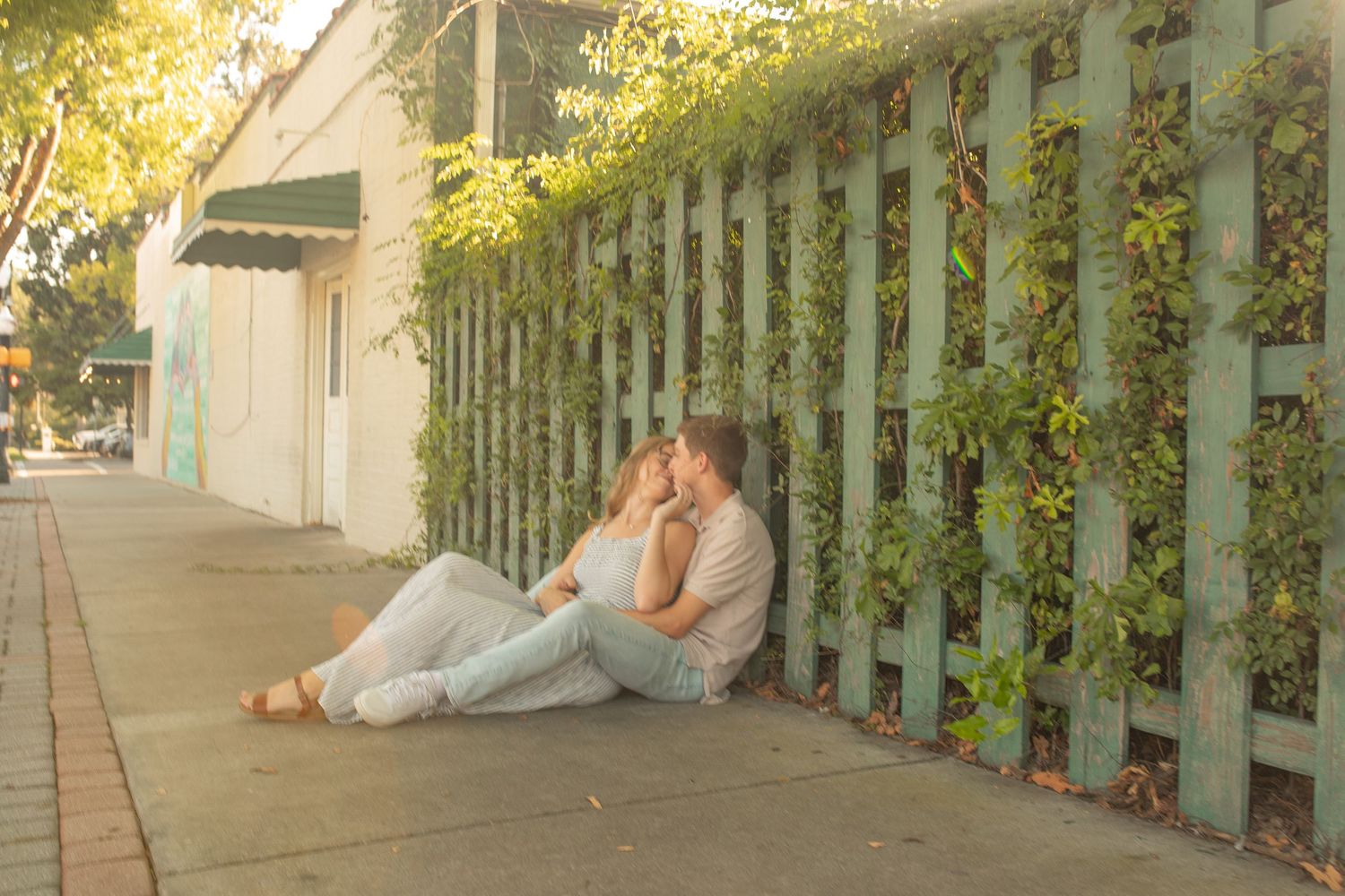 A couple sits together by a white picket fence with climbing vines on a sunny afternoon.