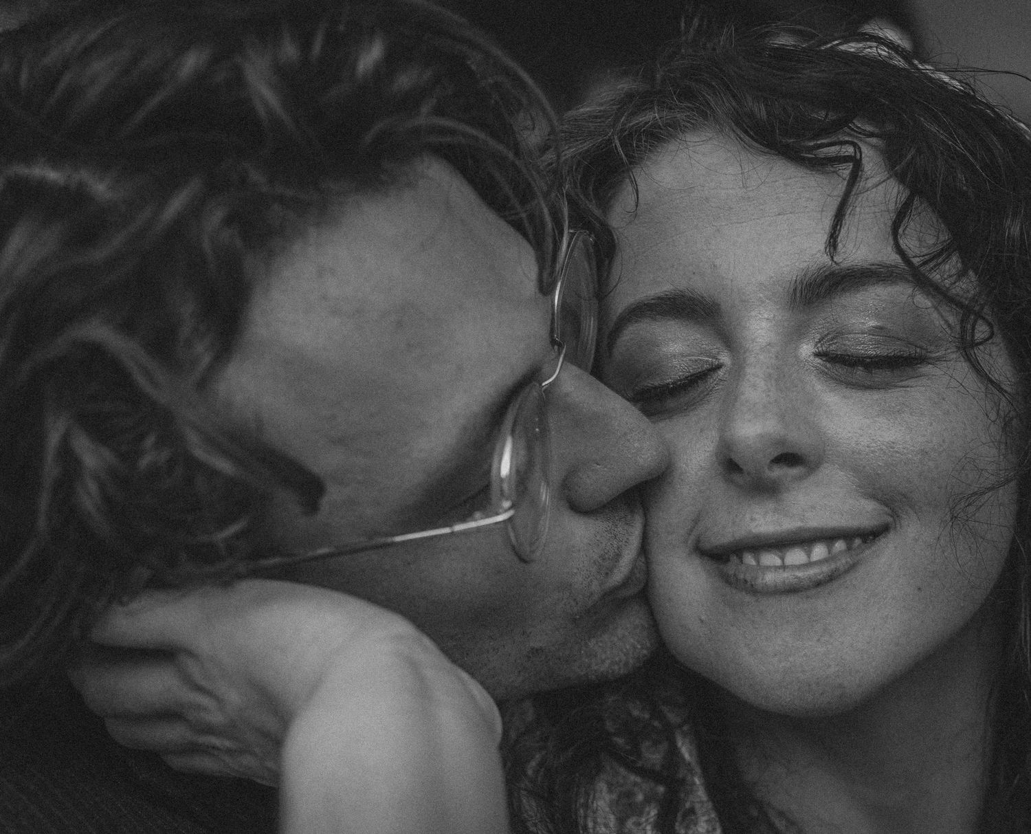 Black and white photo of a couple sharing a tender moment, man kissing smiling woman's cheek.