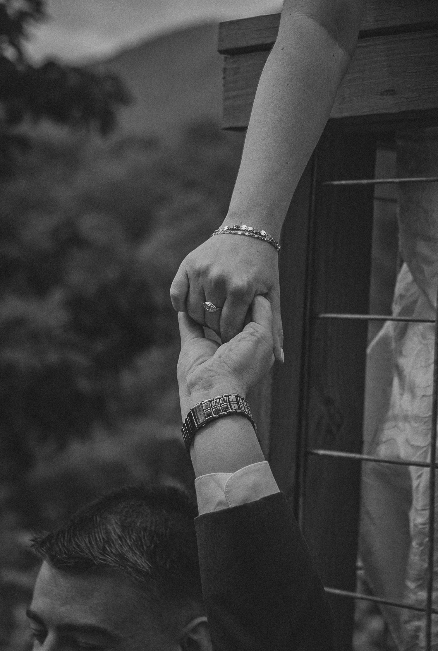 Black and white photo of a couple holding hands, man wearing a watch, woman with a bracelet and ring.