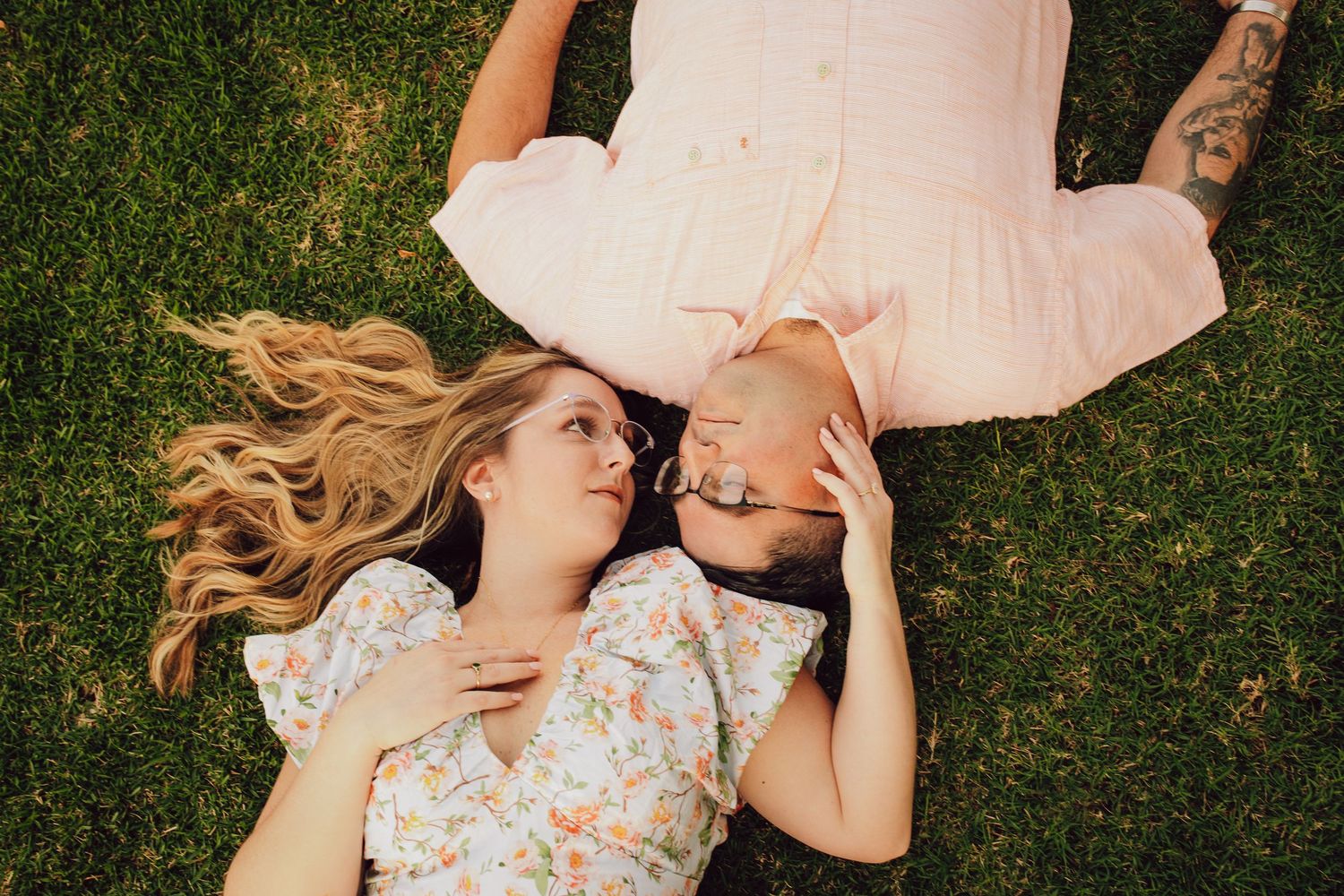 A couple lying on grass together with flowing blonde hair spread out.